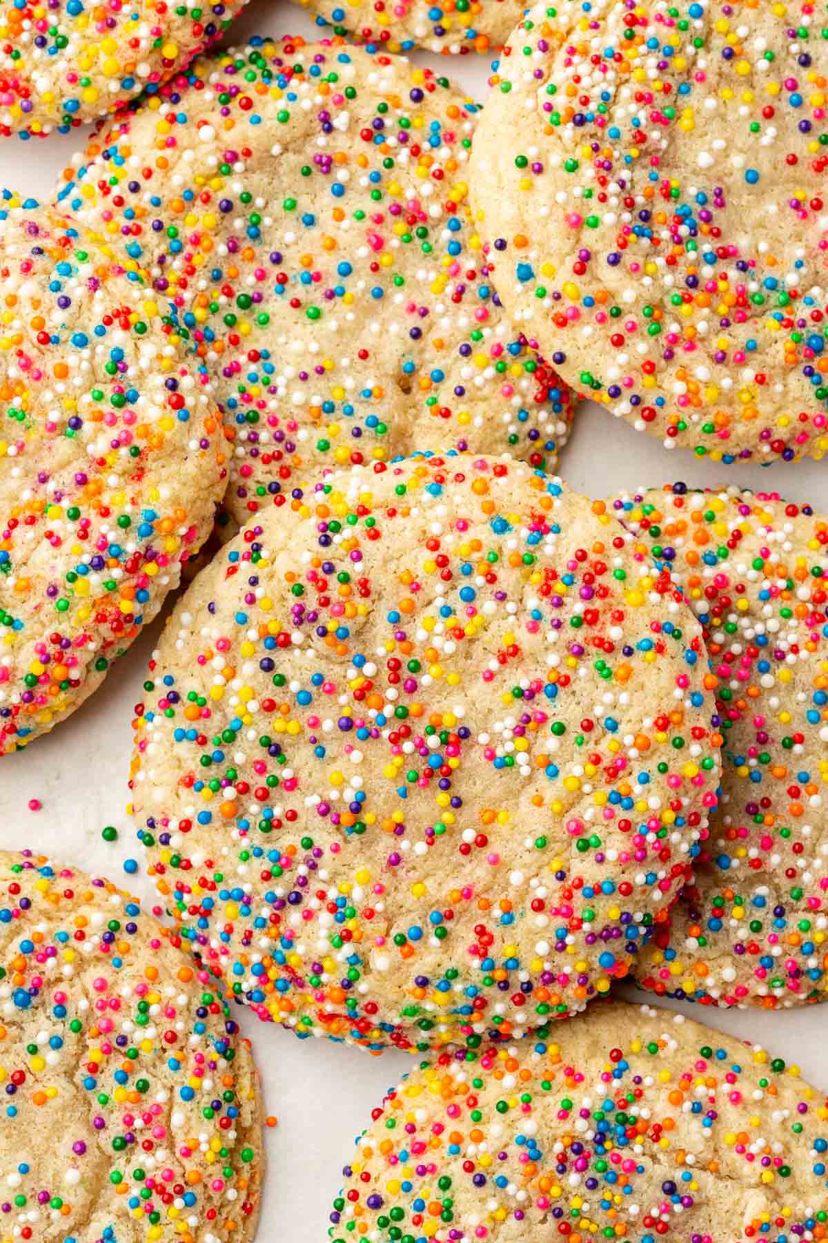 Gluten-free sprinkles sugar cookies overlapping each other on a piece of parchment paper.