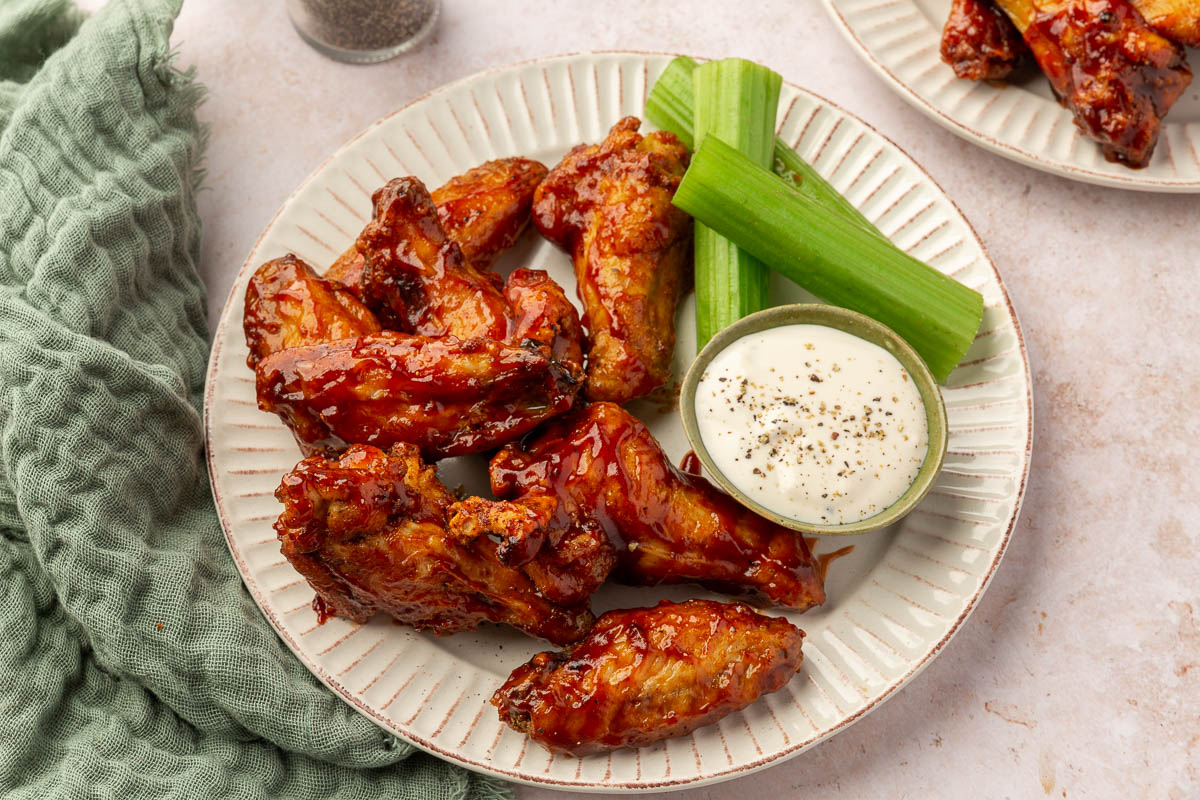 A plate of BBQ chicken wings with a side of celery sticks and a small bowl of bleu cheese dressing.