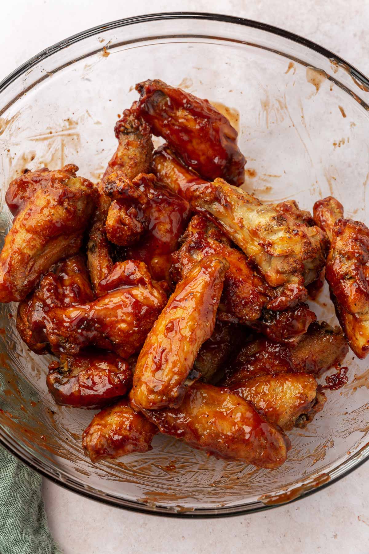 A glass mixing bowl with gluten-free baked chicken wings that have been tossed in BBQ sauce.