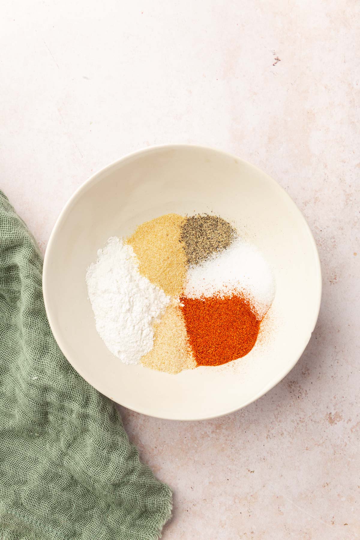 A small white bowl filled with baking powder, garlic powder, pepper, salt, paprika and onion powder before mixing together.