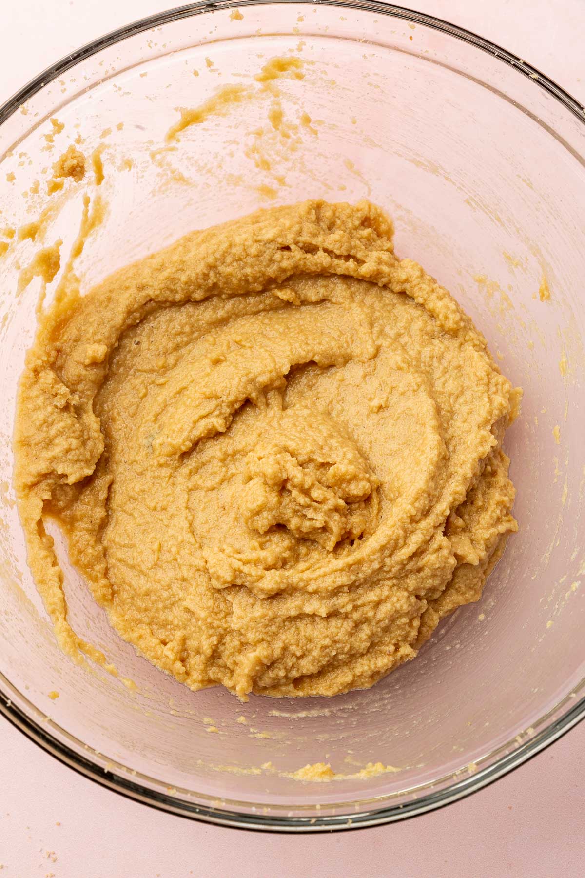 A glass mixing bowl with a creamed butter and brown sugar mixture that has been mixed together with eggs and vanilla extract.