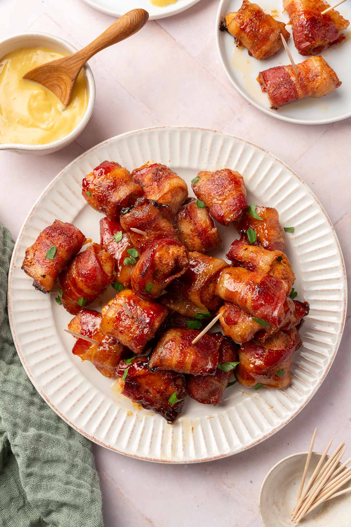 An overhead view of a plate of bacon wrapped chicken bite appetizers with a bowl of honey mustard to the side and some toothpicks.
