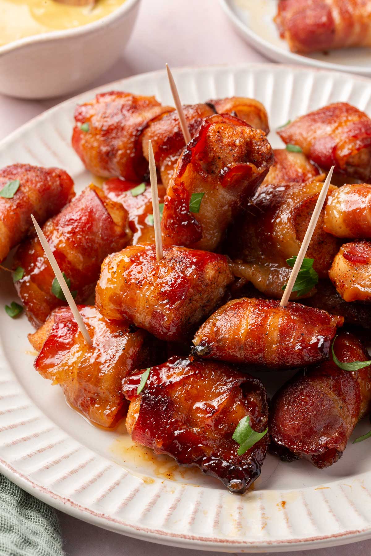 Bacon wrapped chicken appetizers in a pile on a plate with toothpicks stuck in them.