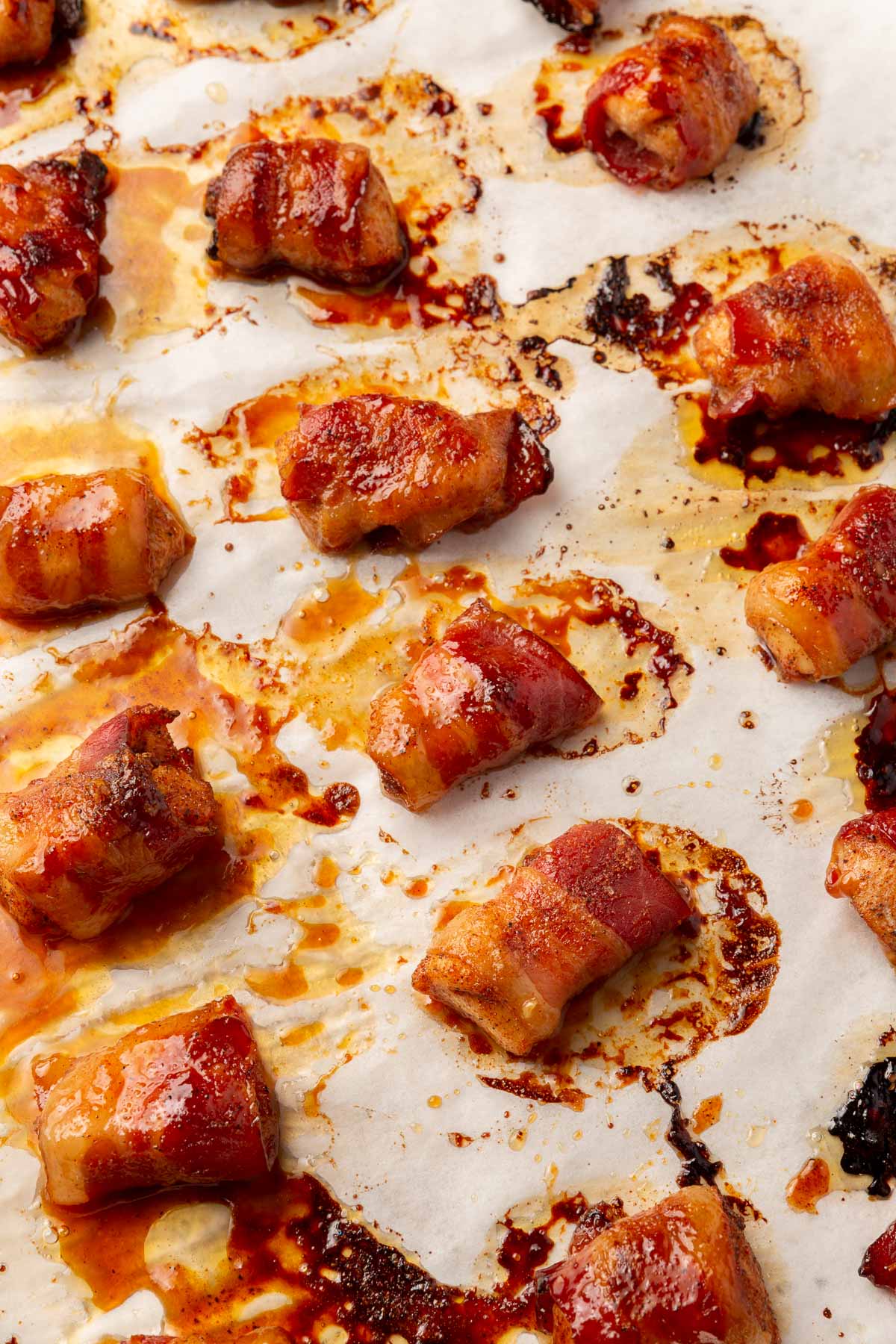 Rows of brown sugar bacon wrapped chicken bites on a piece of parchment paper that have been baked in the oven.