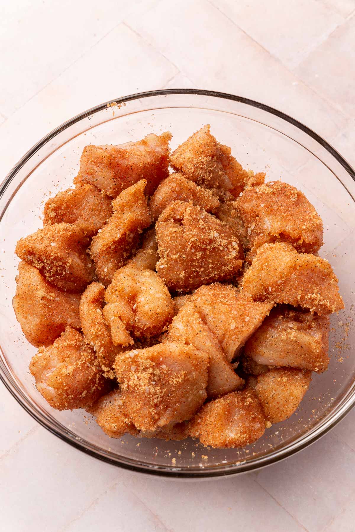 A glass mixing bowl of cubed chicken breast tossed in a spiced brown sugar mixture.