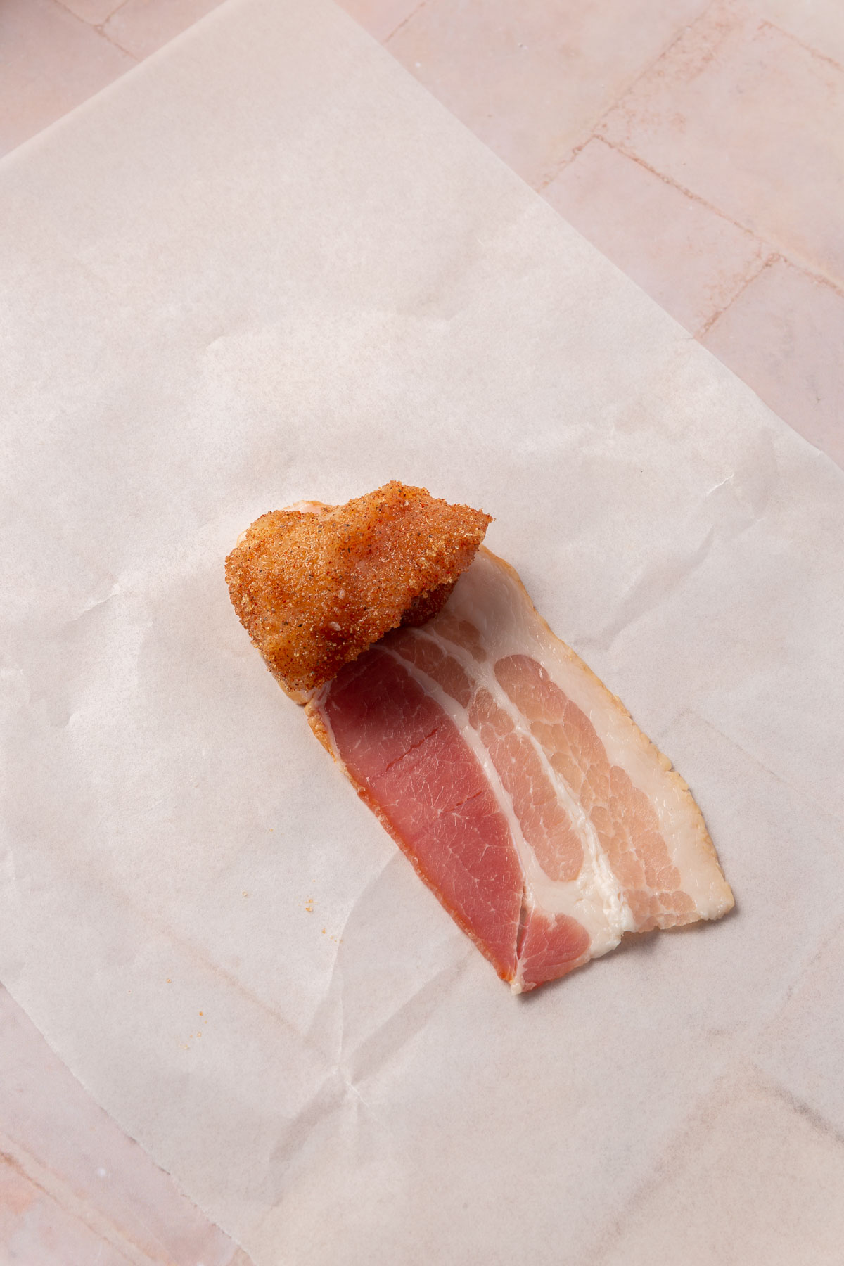 A brown sugar coated piece of chicken breast on top of a piece of bacon.