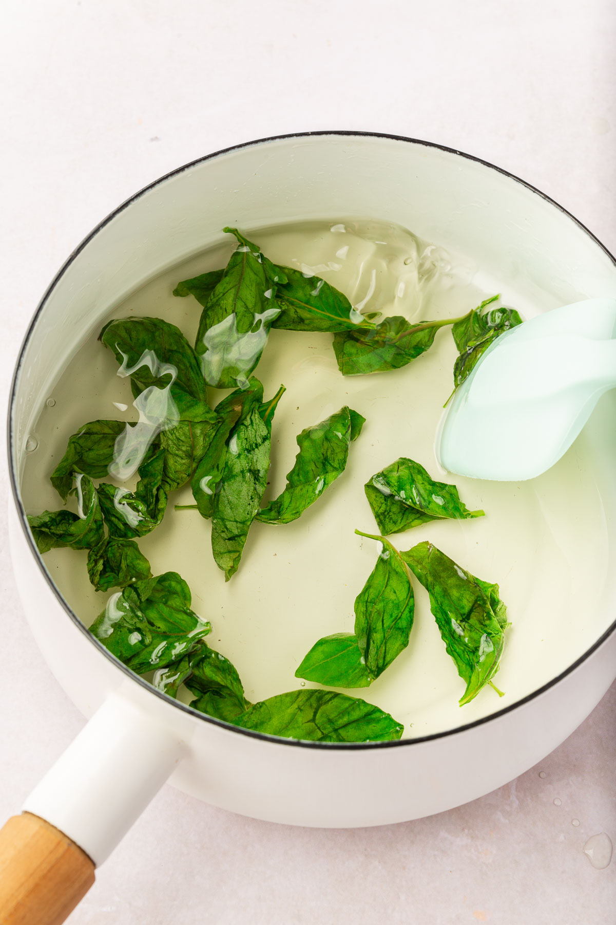 A saucepan of basil simple syrup being stirred by a silicone spatula.