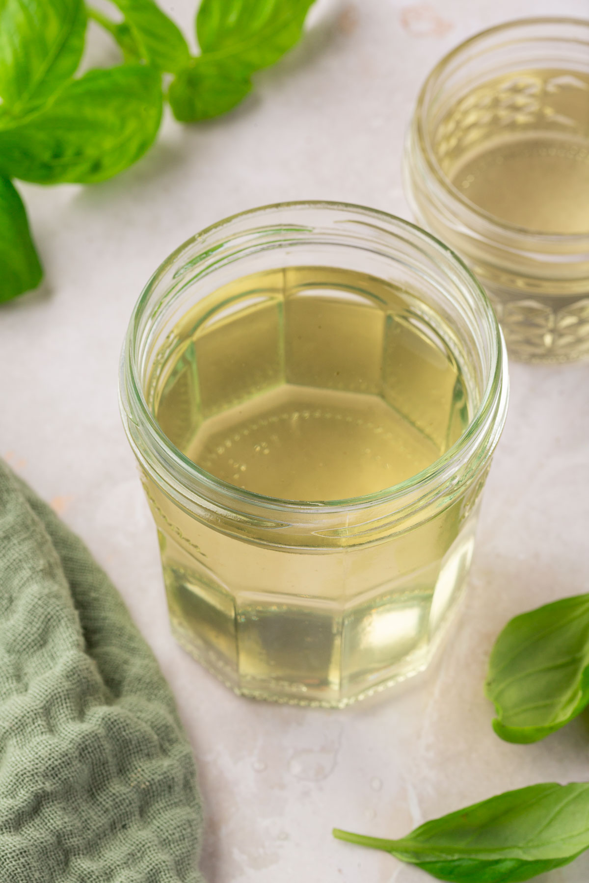A glass jar of basil simple syrup with fresh basil leaves surrounding it.