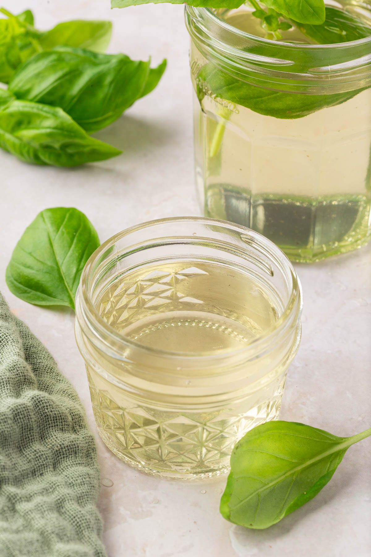 Two jars of basil simple syrup with fresh basil leaves surrounding them.