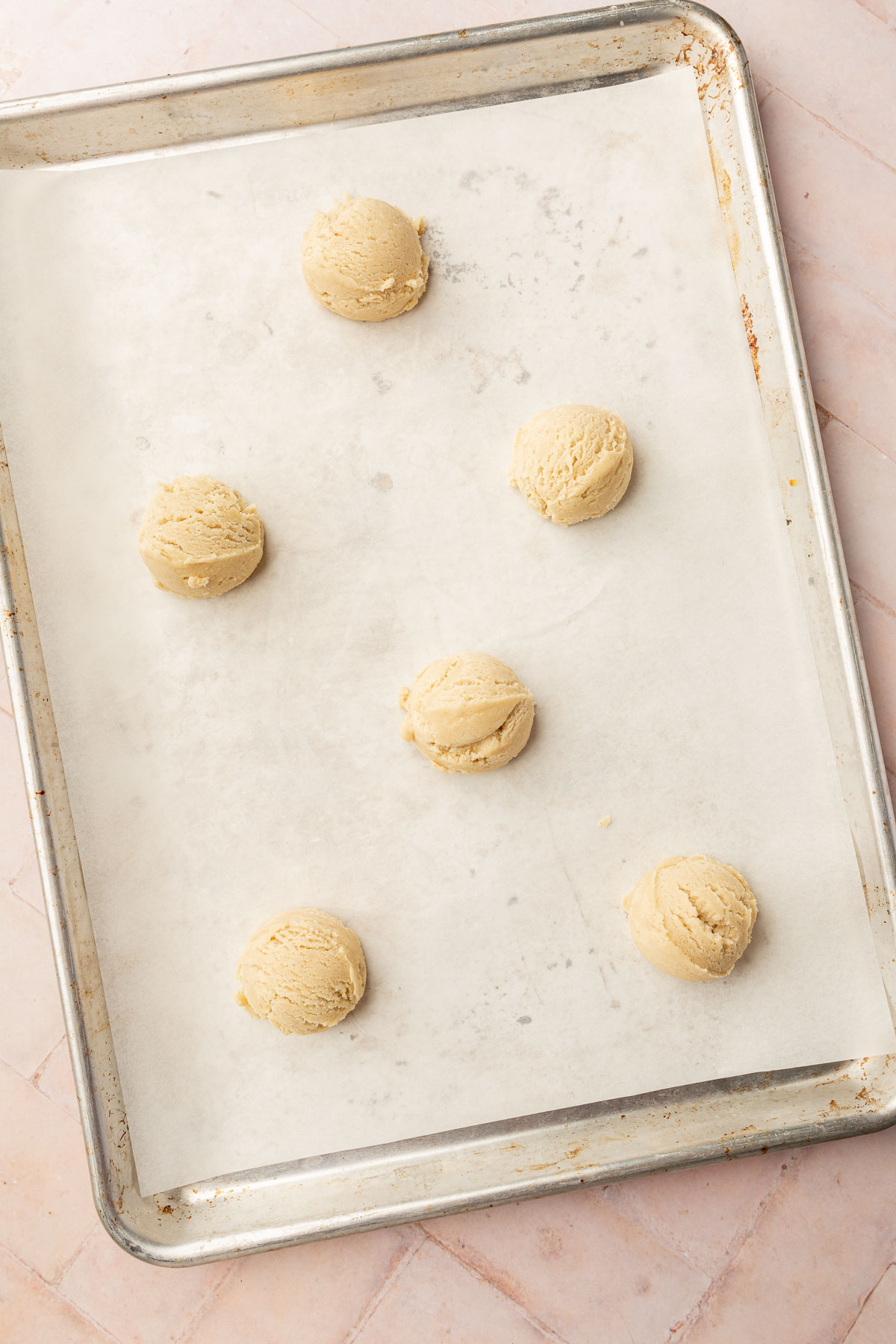 A baking sheet lined with parchment paper and topped with 6 gluten free sugar cookie dough balls before baking in the oven.