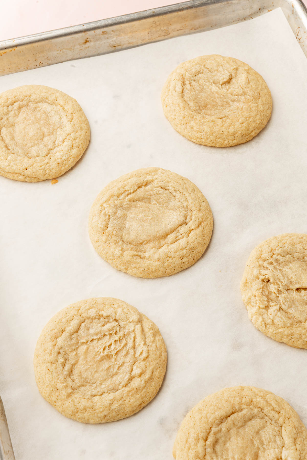 A baking sheet lined with parchment paper and topped with six gluten free chewy sugar cookies after baking in the oven.