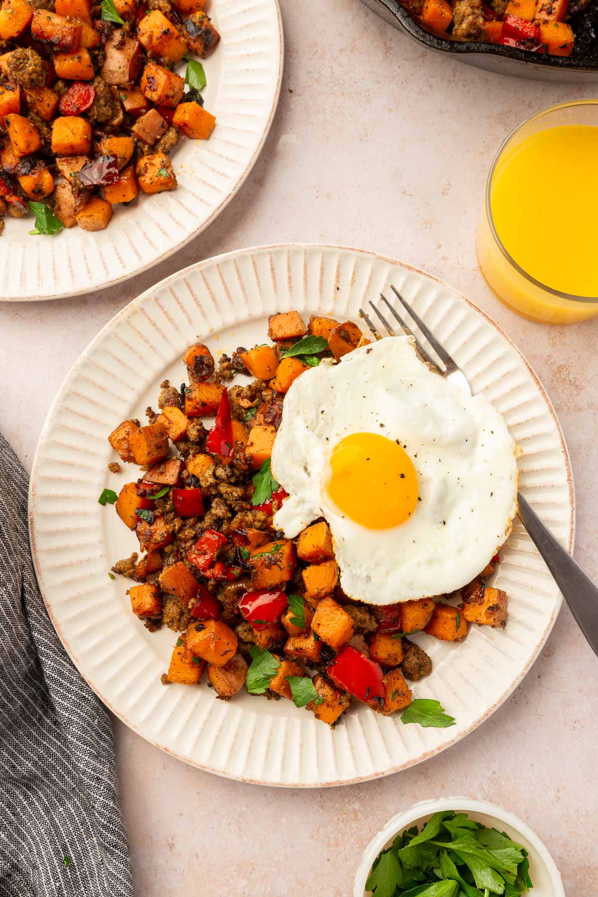 Multiple plates of sweet potato hash with an egg on top with a glass of orange juice to the side.