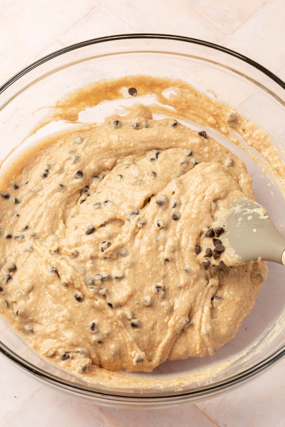 A glass mixing bowl with gluten-free chocolate chip coffee cake batter and a spatula.