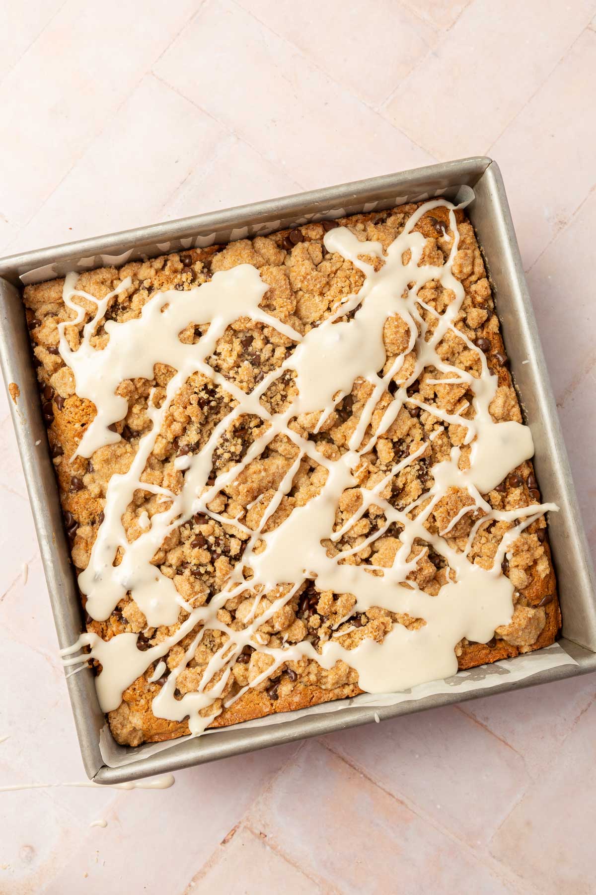 An overhead view of a square baking pan filled with glute-free chocolate c chip coffee cake with a vanilla glaze drizzle and gluten-free streusel.