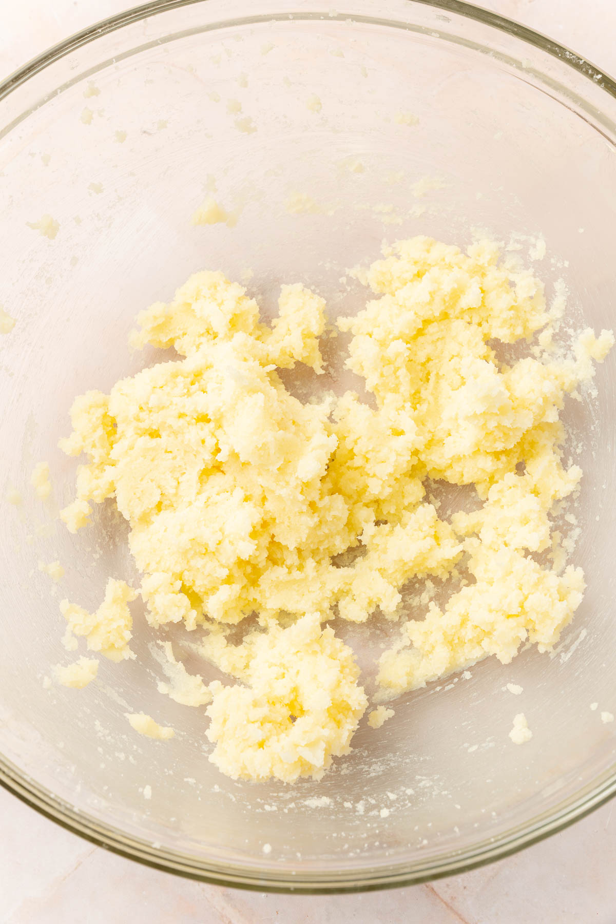 A glass mixing bowl with creamed butter and granulated sugar in it.