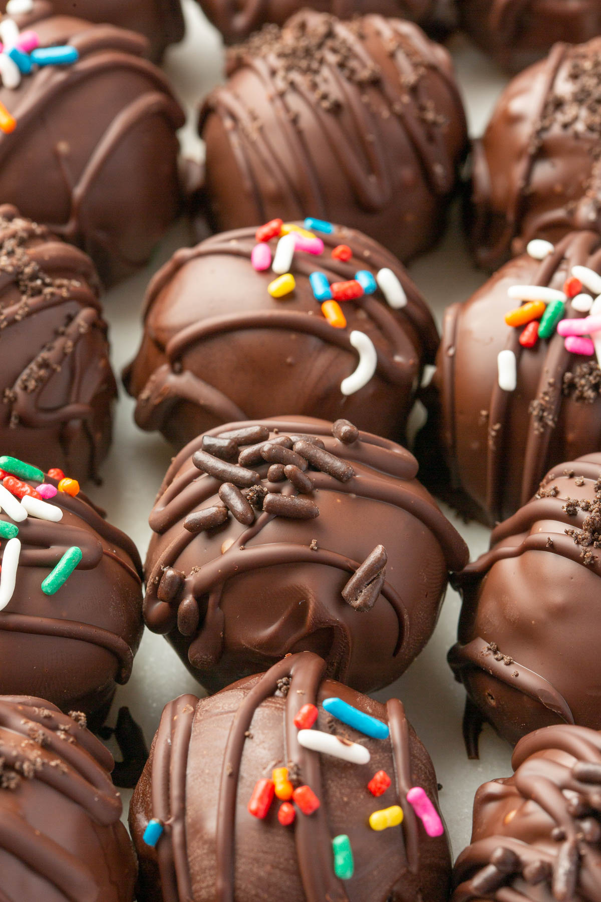 A close up of a dozen gluten-free Oreo balls in rows dipped in semi-sweet chocolate with various different sprinkles on top each one.