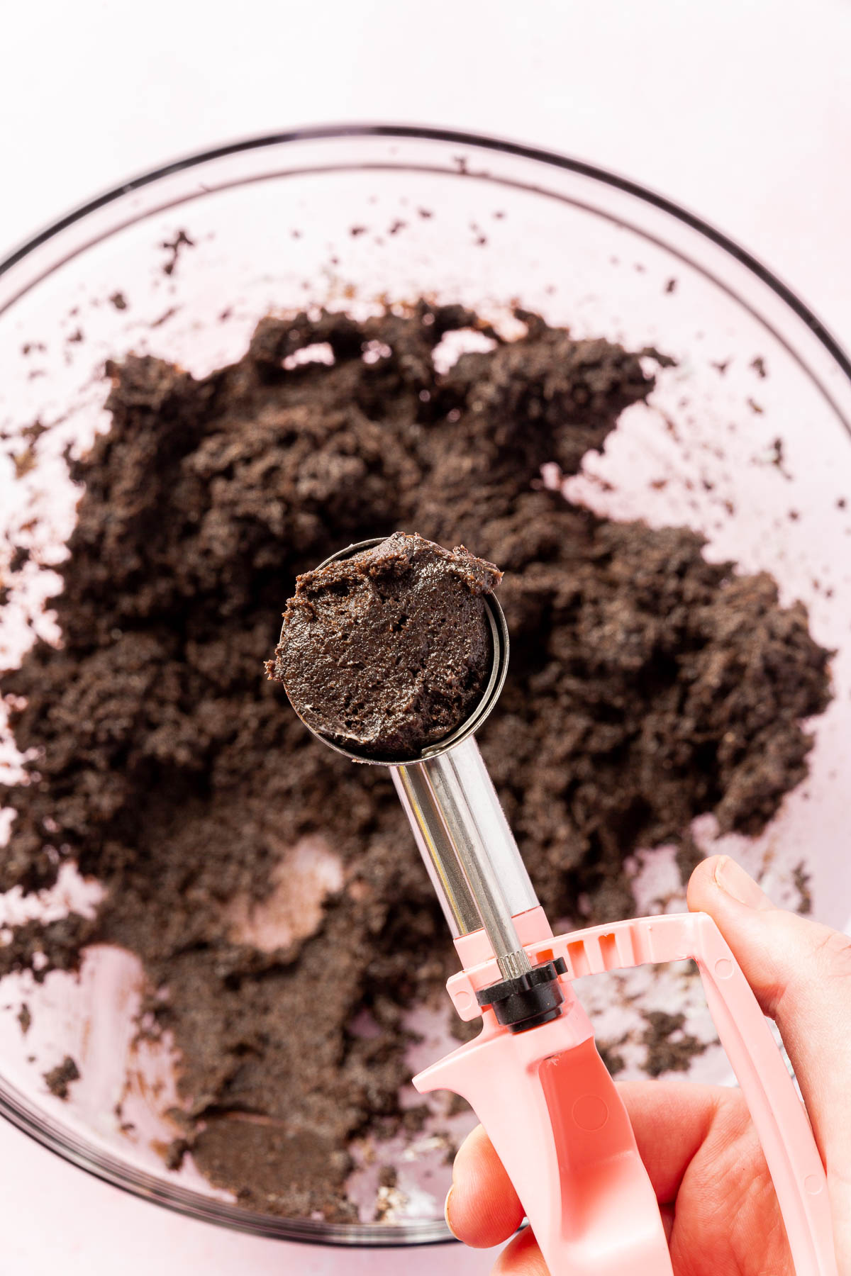 A small portion scooper filled with gluten-free Oreo cheesecake ball dough over a mixing bowl of additional Oreo truffle mixture.