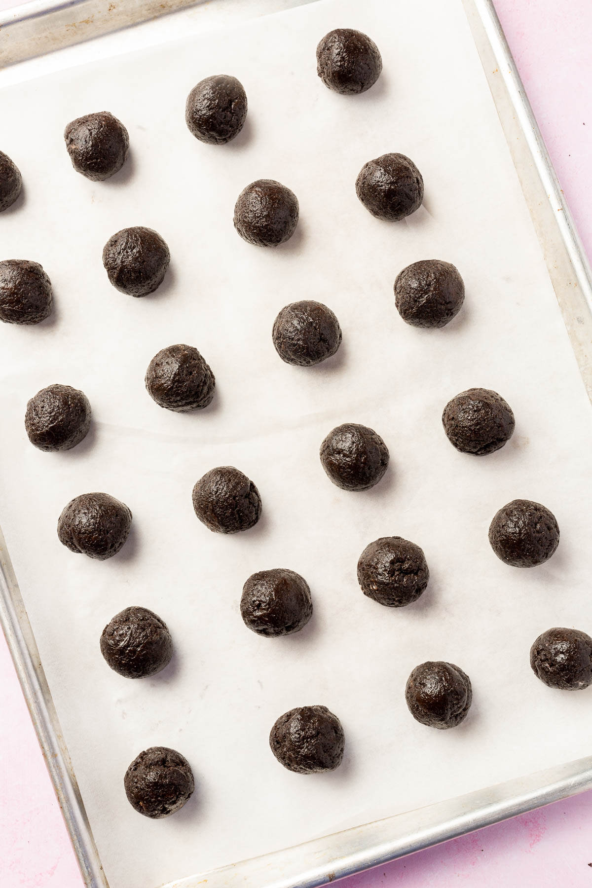 A baking sheet lined with parchment paper with rows of Oreo balls on it before dipping into semi-sweet chocolate.
