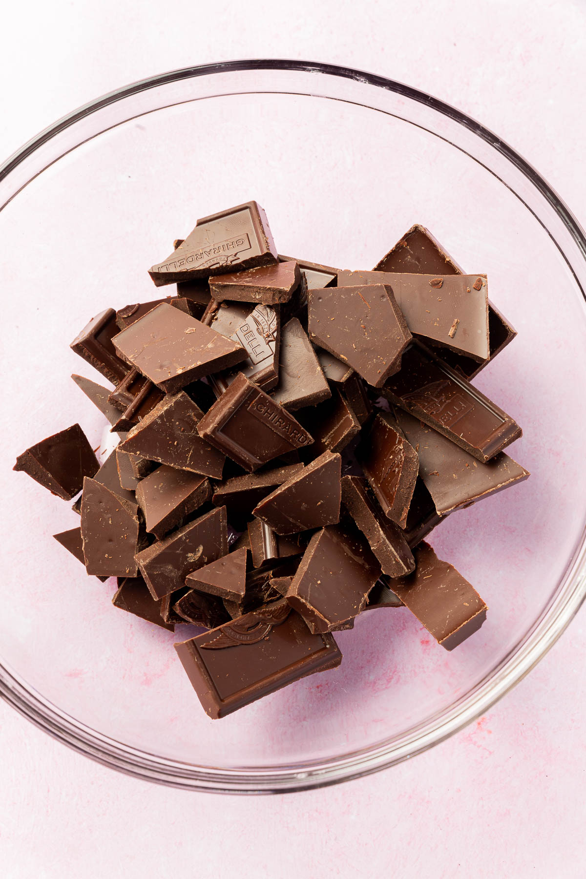 A glass mixing bowl with broken up pieces of semi-sweet chocolate in it.