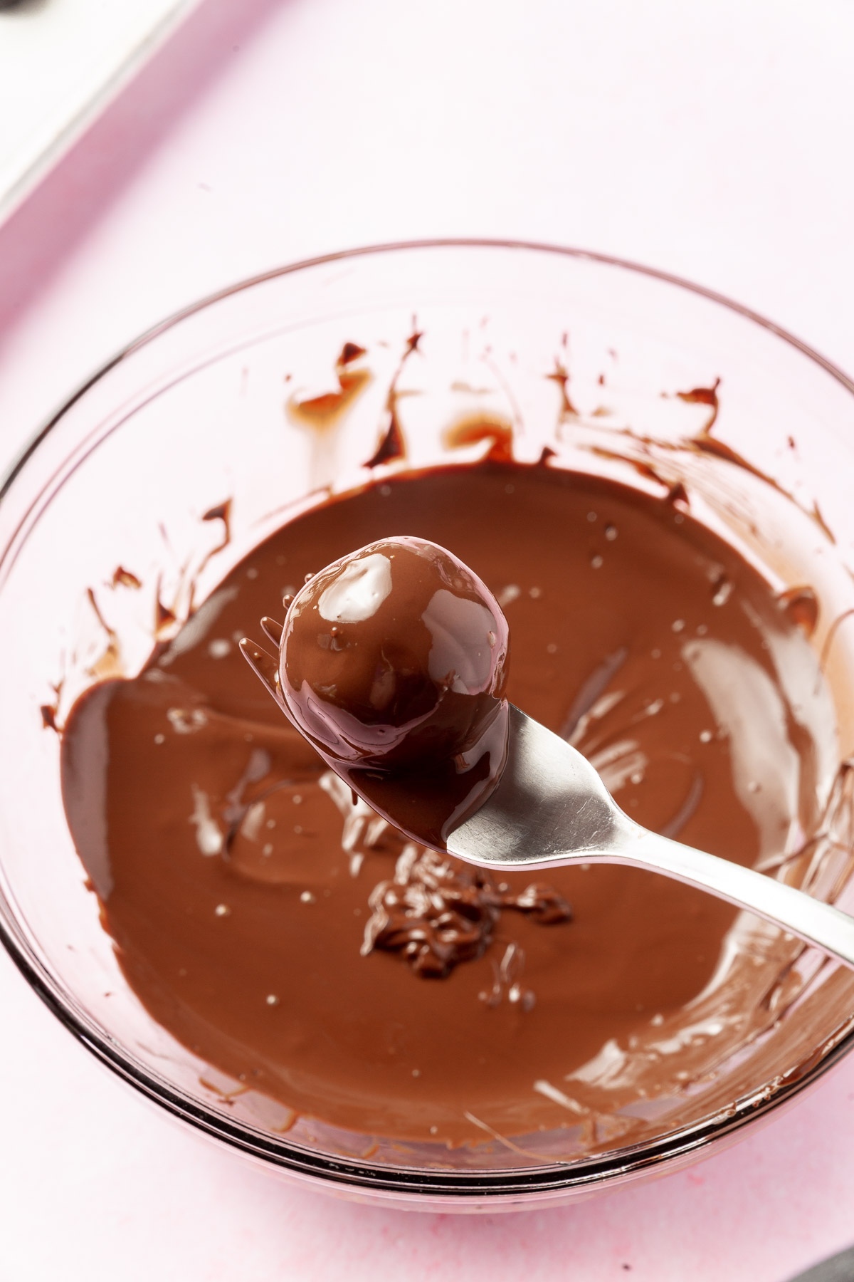 A single Oreo ball that has been dipped in a bowl of melted semi-sweet chocolate with a fork.