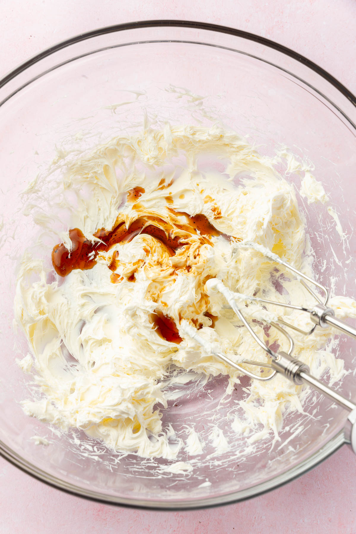 A mixing bowl with cream cheese and vanilla extract before mixing together with an electric mixer.