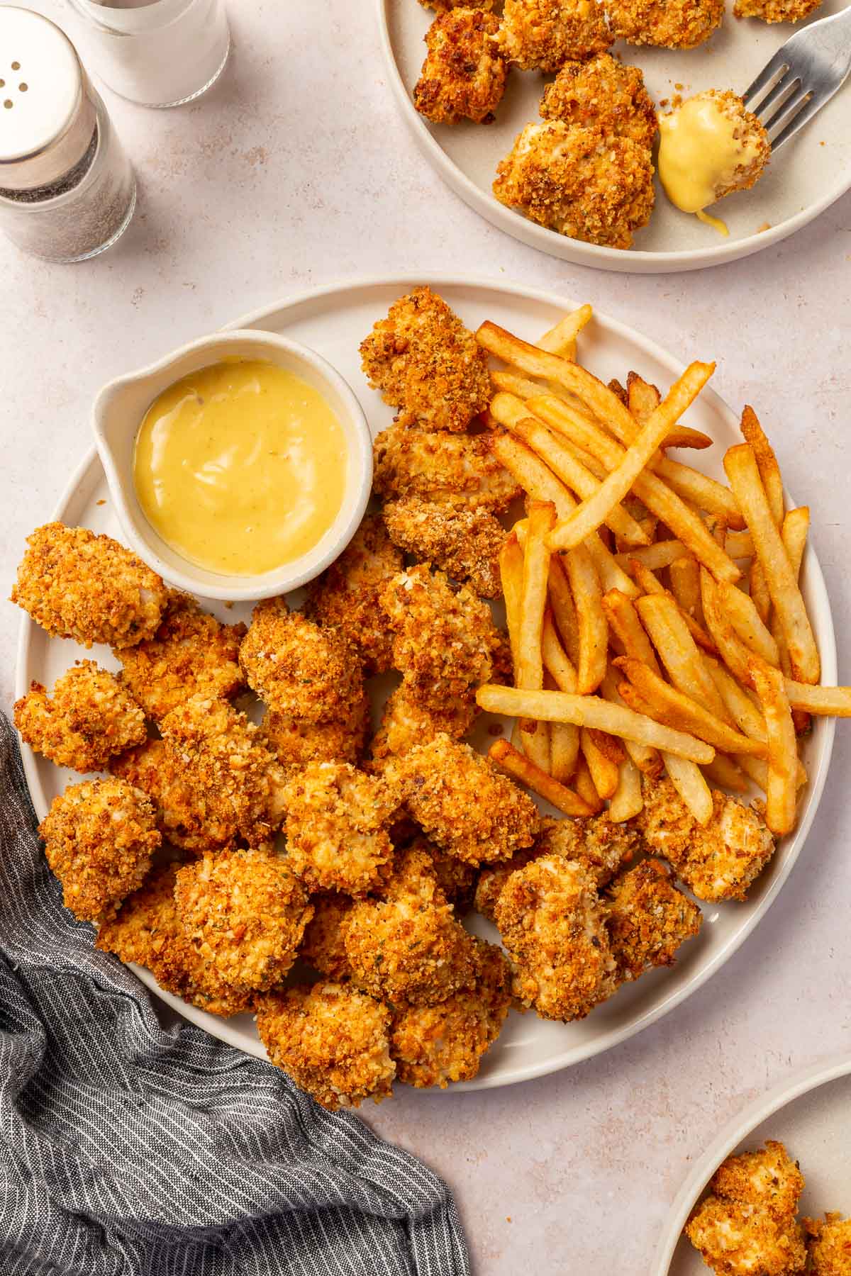 An overhead platter of gluten-free chicken nuggets that were baked in the oven with a side of french fries and a small ramekin of honey mustard dipping sauce with additional plates of chicken nuggets off to the side.