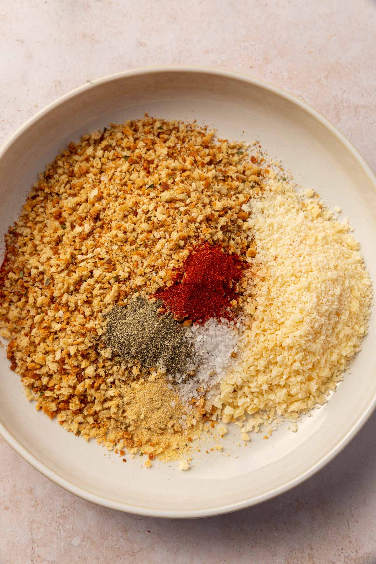 A shallow bowl of gluten-free breadcrumbs, black pepper, paprika, salt, garlic powder and parmesan cheese before whisking together.