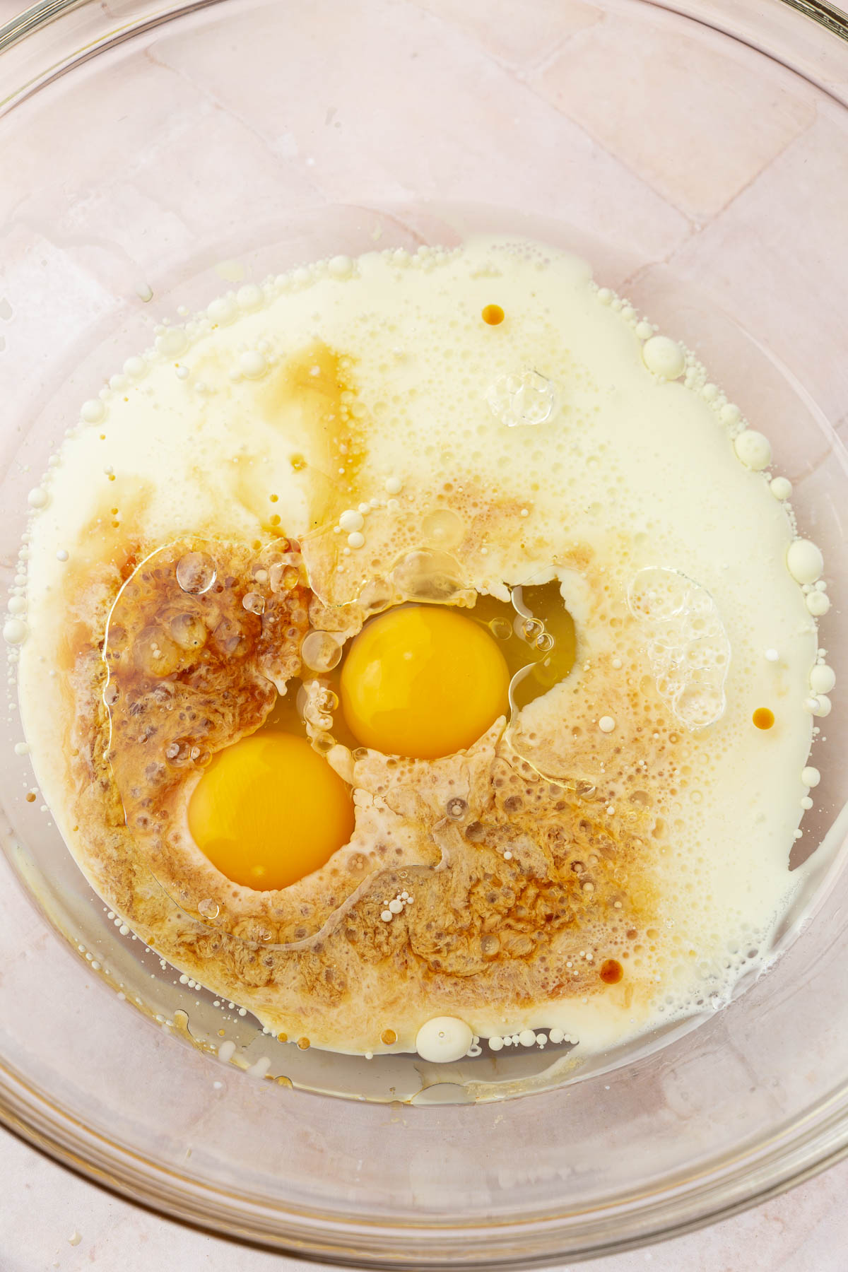 Close-up of a mixing bowl containing wet ingredients for gluten-free chocolate muffins, including eggs, milk, vanilla extract, and oil.