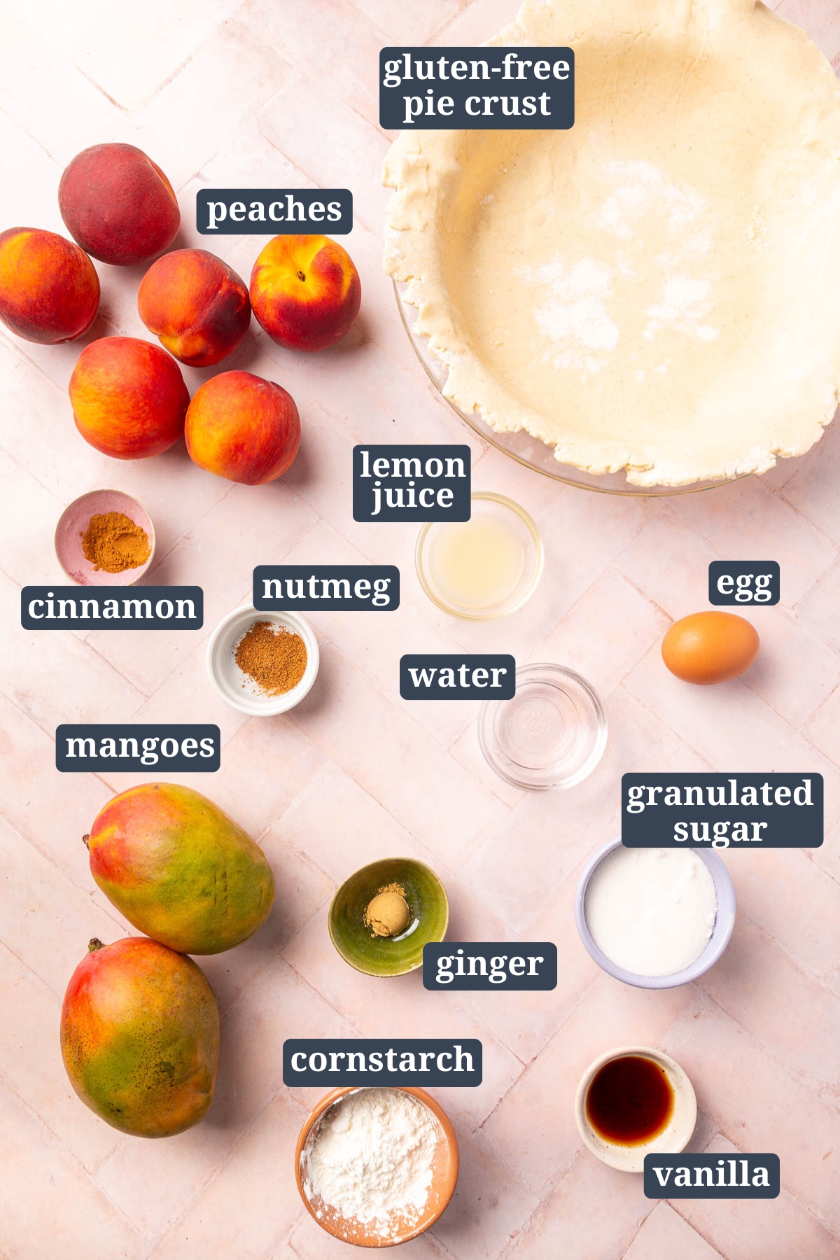 An overhead view of ingredients to make a gluten-free peach mango pie including peaches, a gluten-free pie crust, lemon juice, cinnamon, nutmeg, water, egg, ginger, mangoes, granulated sugar, cornstarch and vanilla.
