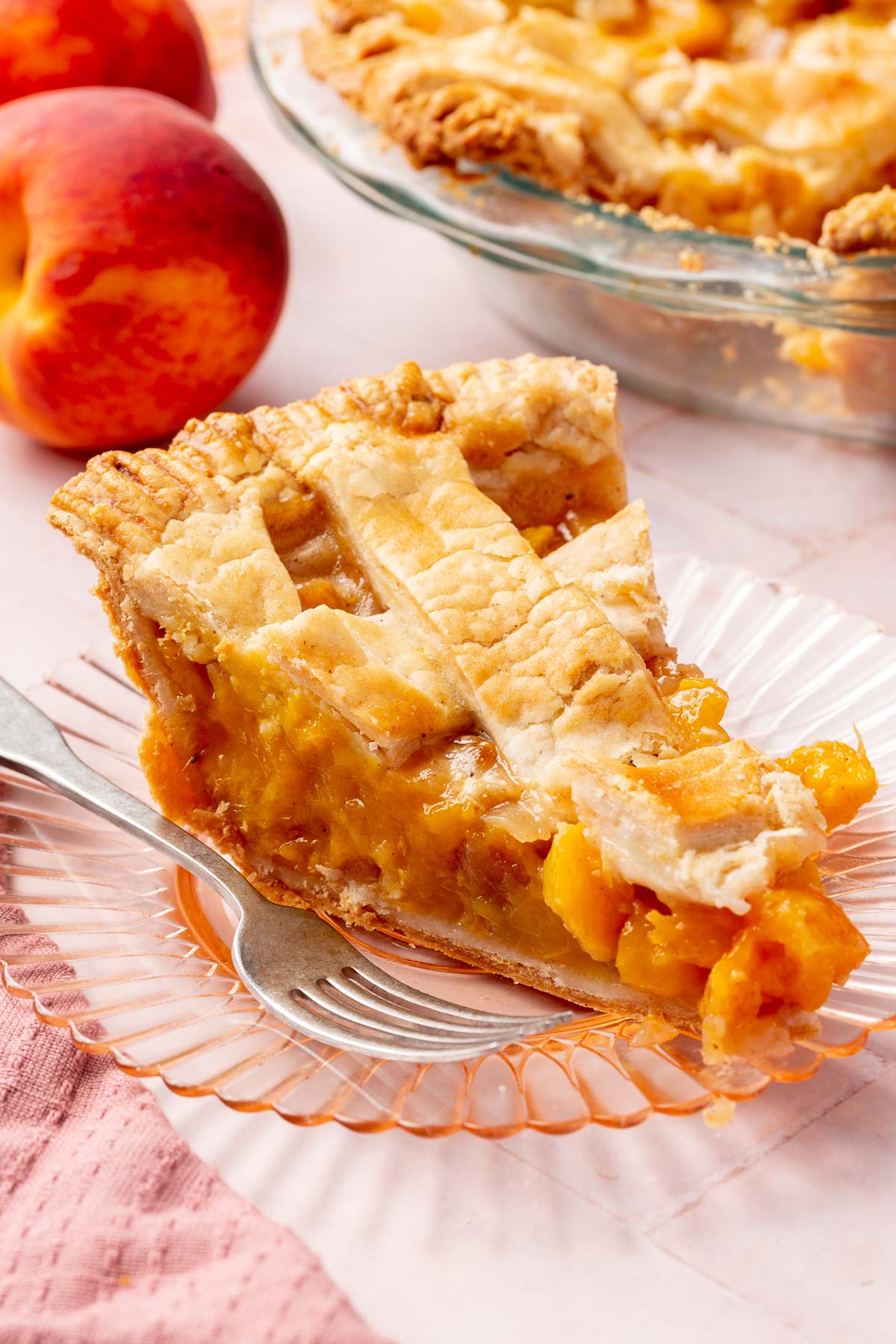 A single slice of gluten-free peach mango pie on a dessert plate with additional pie and peaces in the background.
