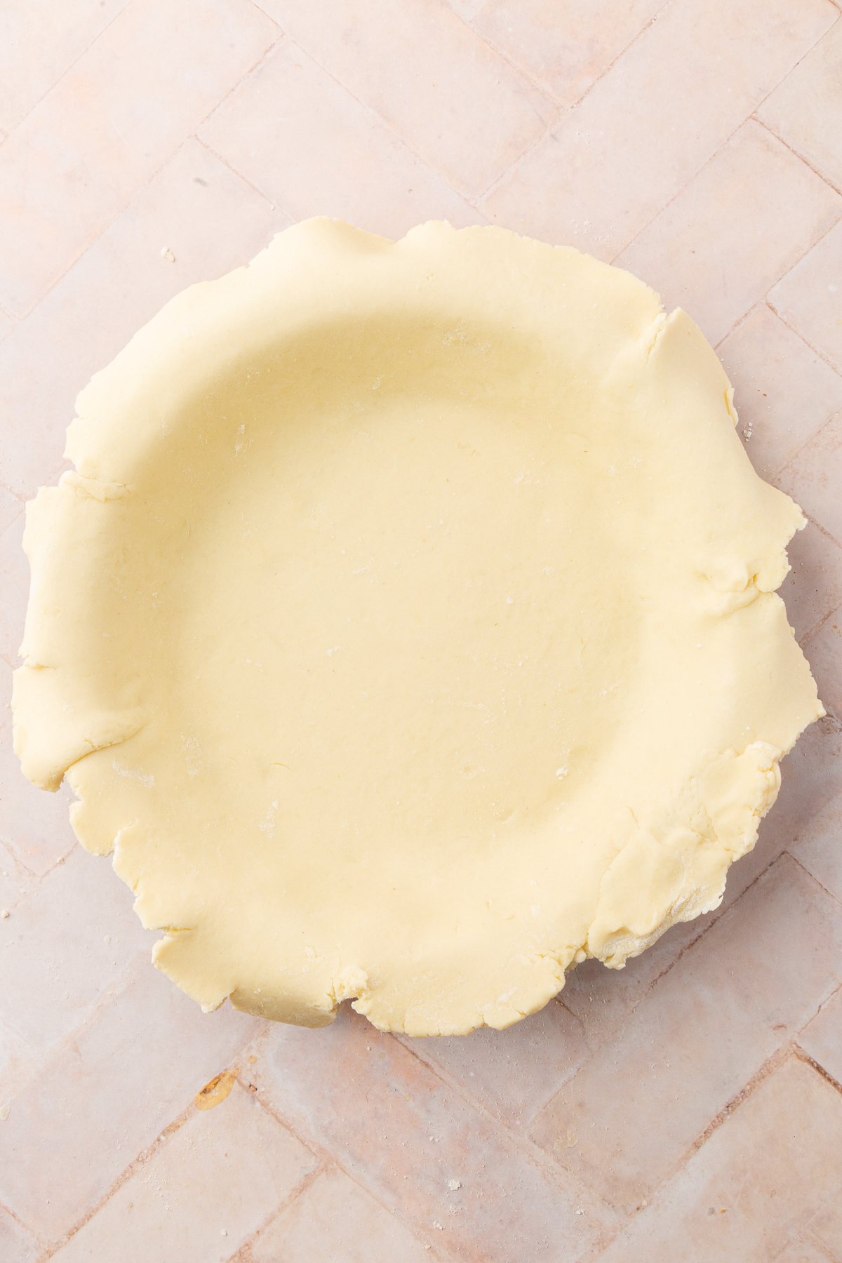 An unbaked gluten-free pie crust laid into a pie pan with the edges slightly overhanging.