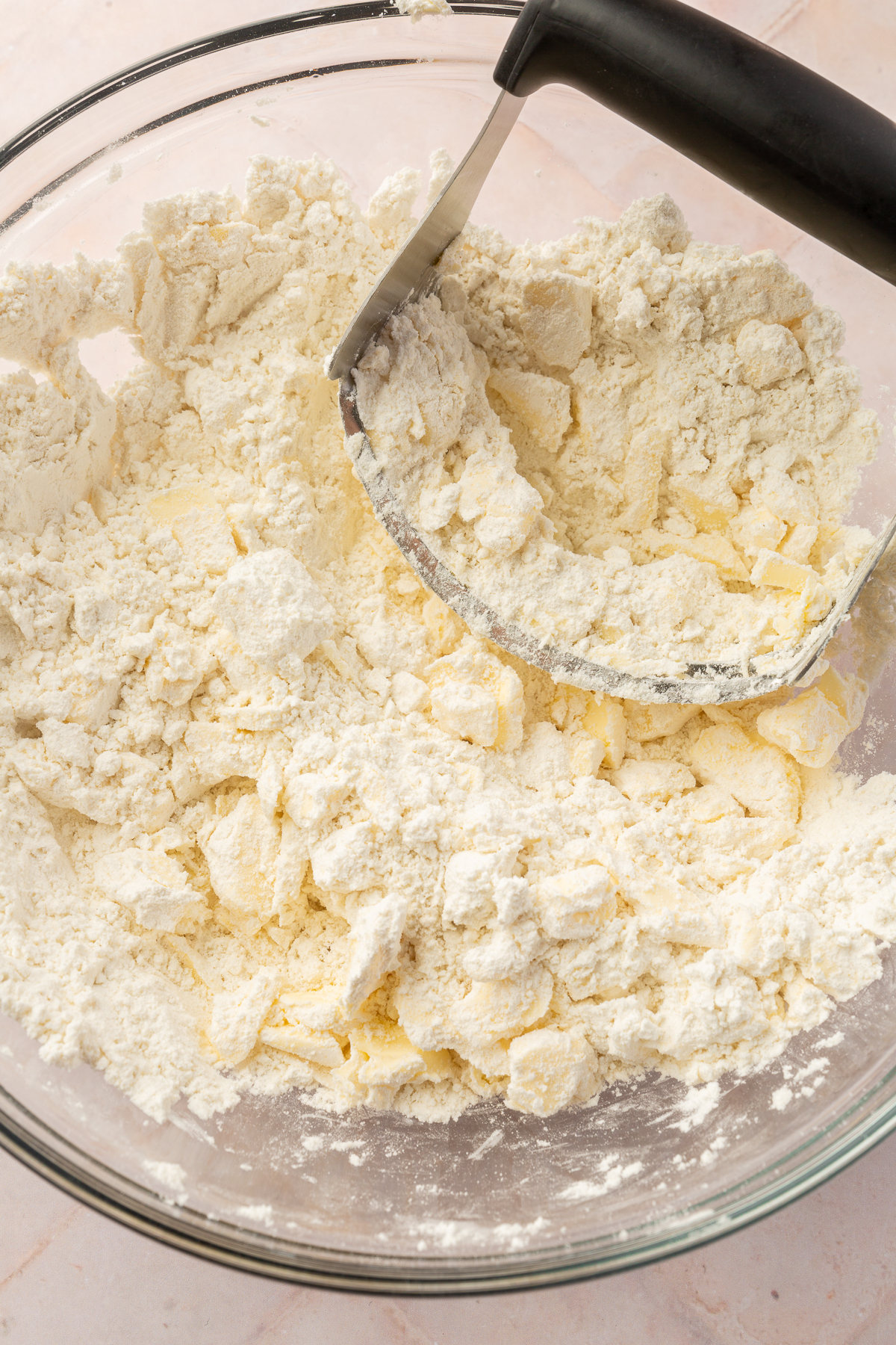 Using a pastry cutter to cut the butter into the gluten-free flour mixture, creating small, pea-sized crumbs essential for a flaky pie crust.