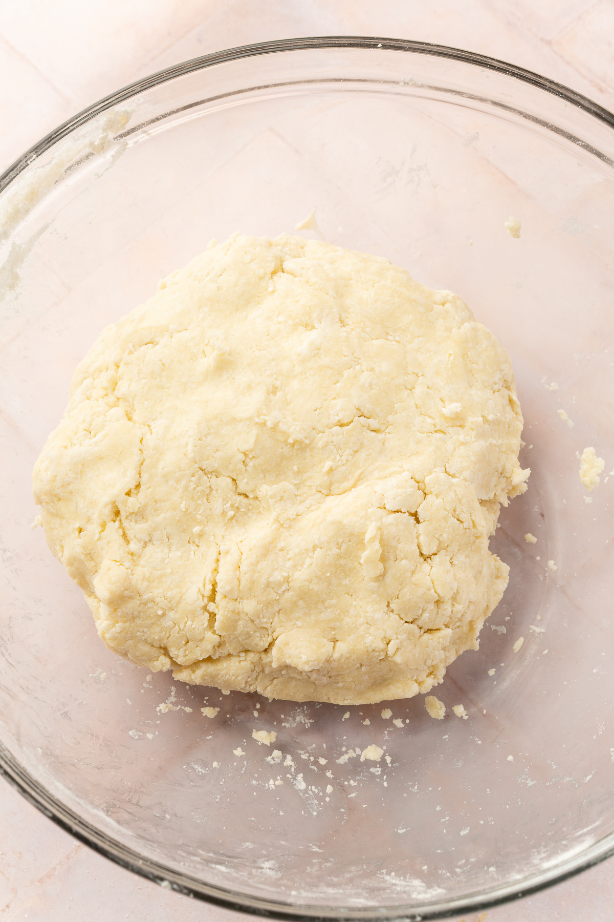 A ball of gluten-free pie dough sits in a glass bowl, fully mixed and ready to be rolled out for a pie crust.