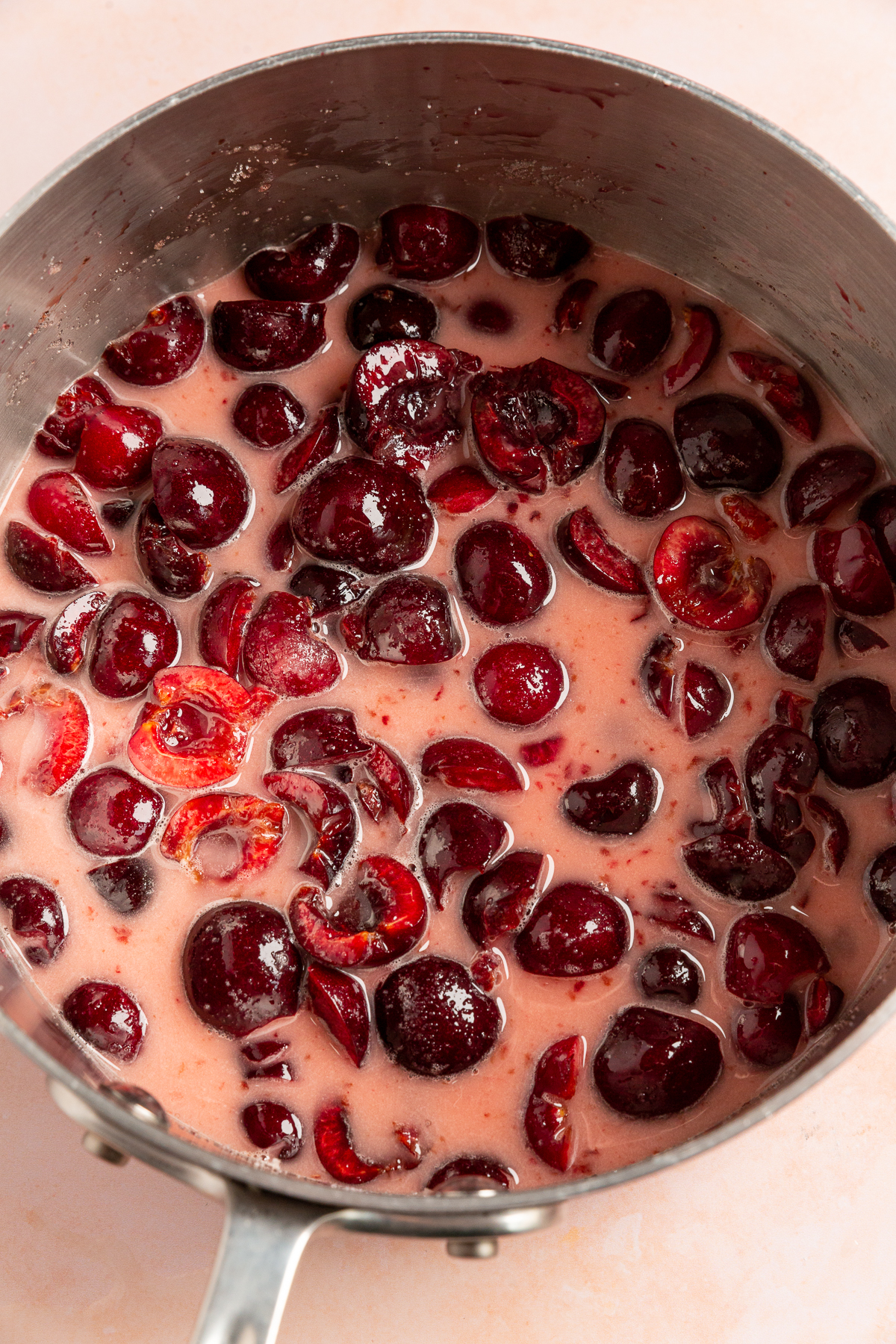A saucepan filled with cherries cooking in their juice and thickening into a pie filling.