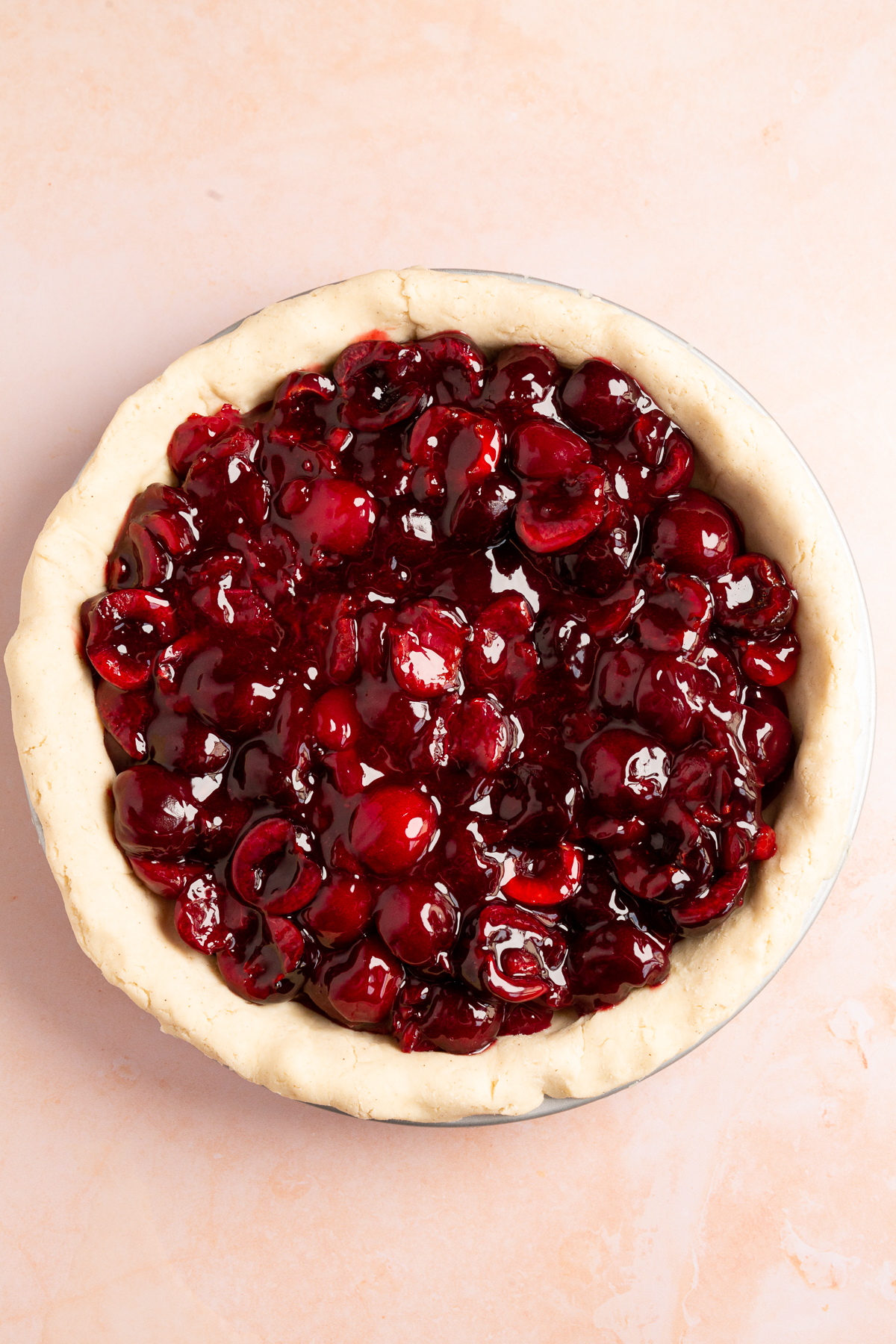 The pie pan filled with rich, glossy cherry pie filling, ready for the top crust to be added.