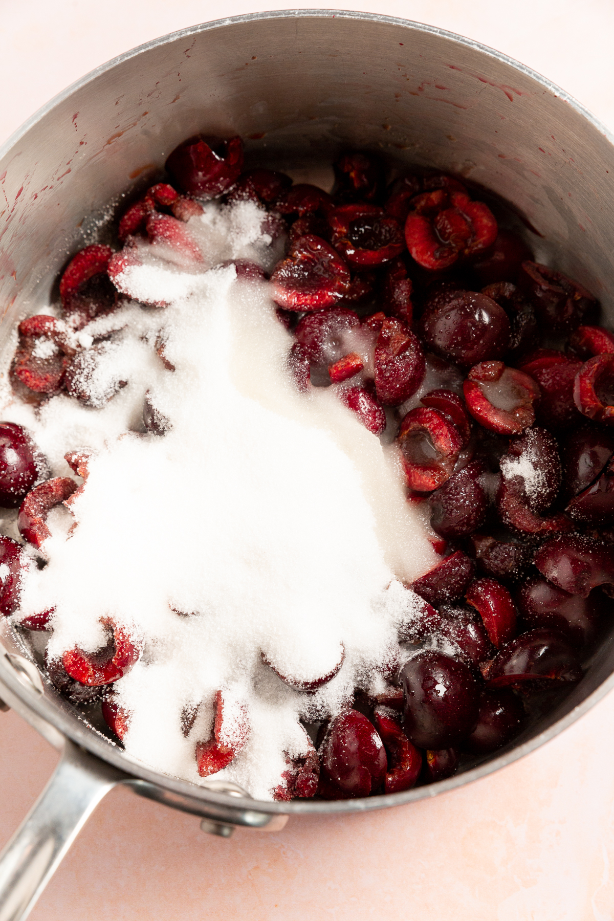 A saucepan filled with pitted cherries and granulated sugar, prepared for cooking the cherry pie filling.