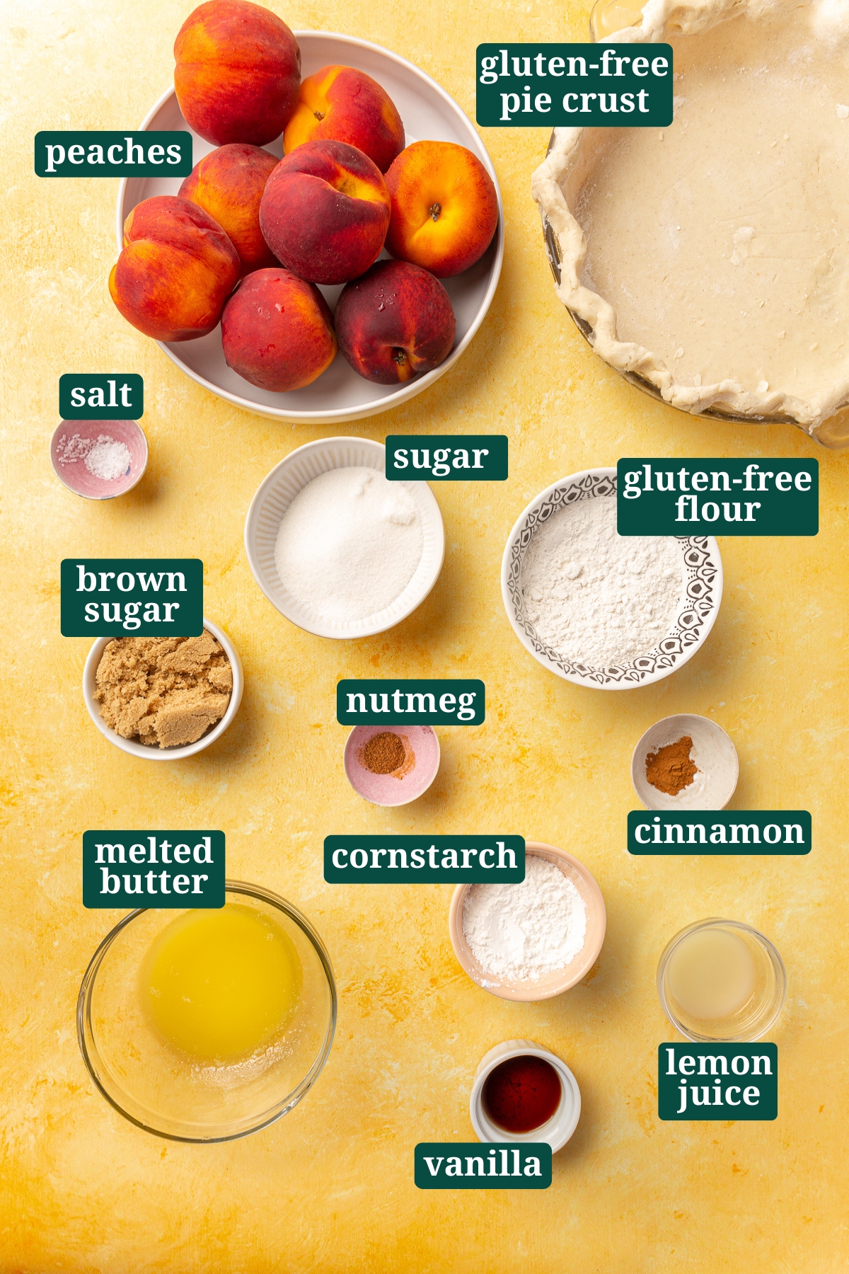 Overhead view of labeled ingredients for a gluten-free peach crumble pie, including peaches, sugar, brown sugar, flour, cinnamon, and nutmeg