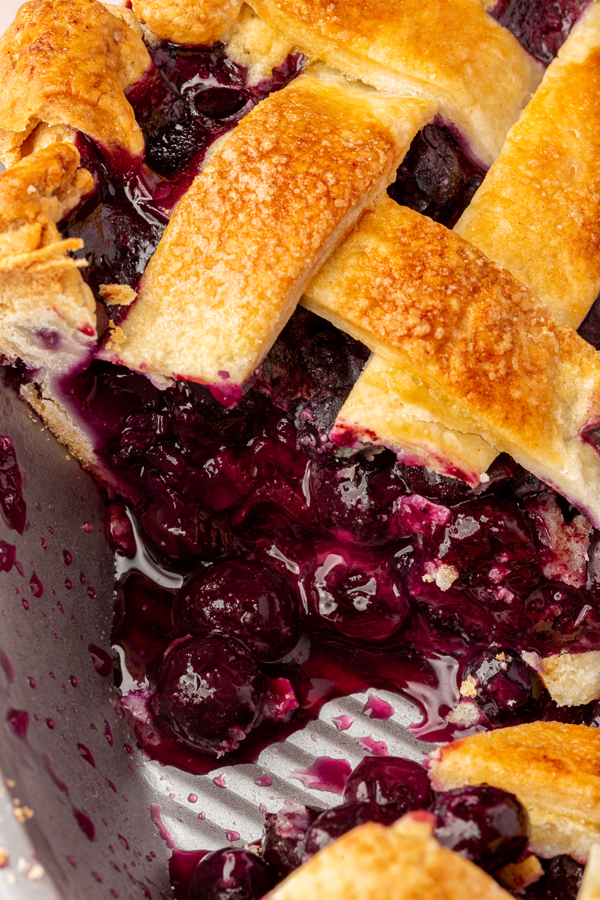 A close-up shot of the blueberry filling inside the pie tin, showing the rich, deep purple blueberry juices spilling out from the flaky crust.