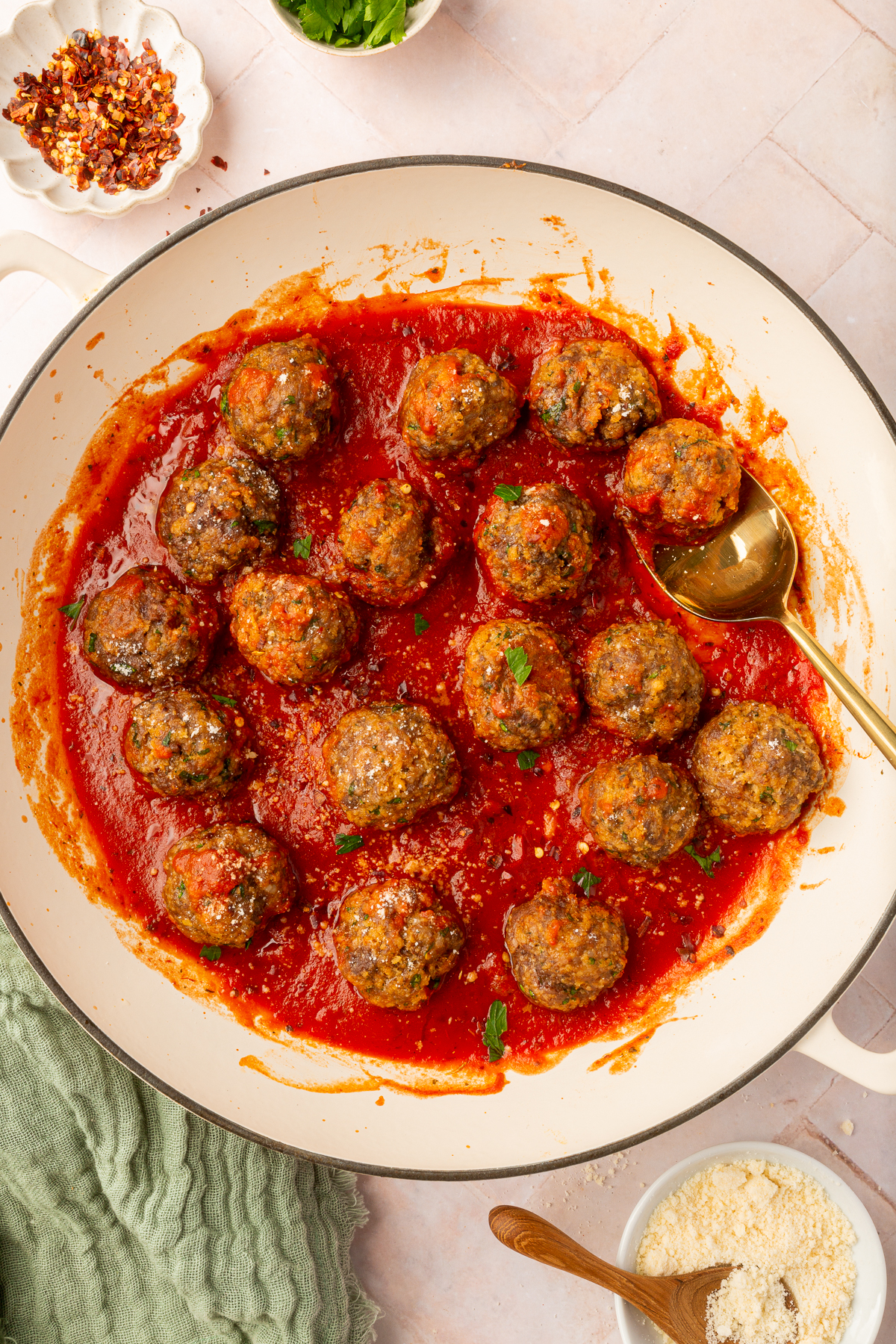 Spicy ground beef, Italian sausage and gluten-free breadcrumb meatballs resting in marinara sauce in a beige bowl on a table with various ingredients.