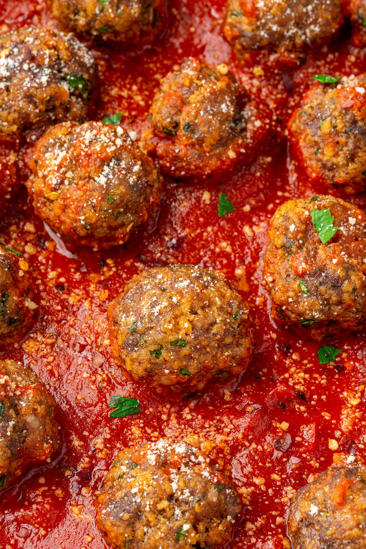 Close up image of spicy ground beef, Italian sausage, and gluten-free breadcrumb meatballs resting in a red marinara sauce.