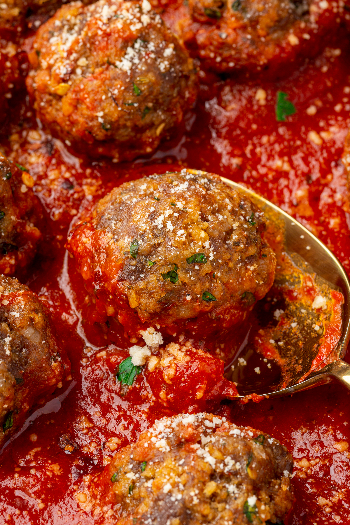 Meatball made with ground beef, Italian sausage and gluten-free breadcrumbs sitting in marinara sauce being scooped up by a metal spoon.