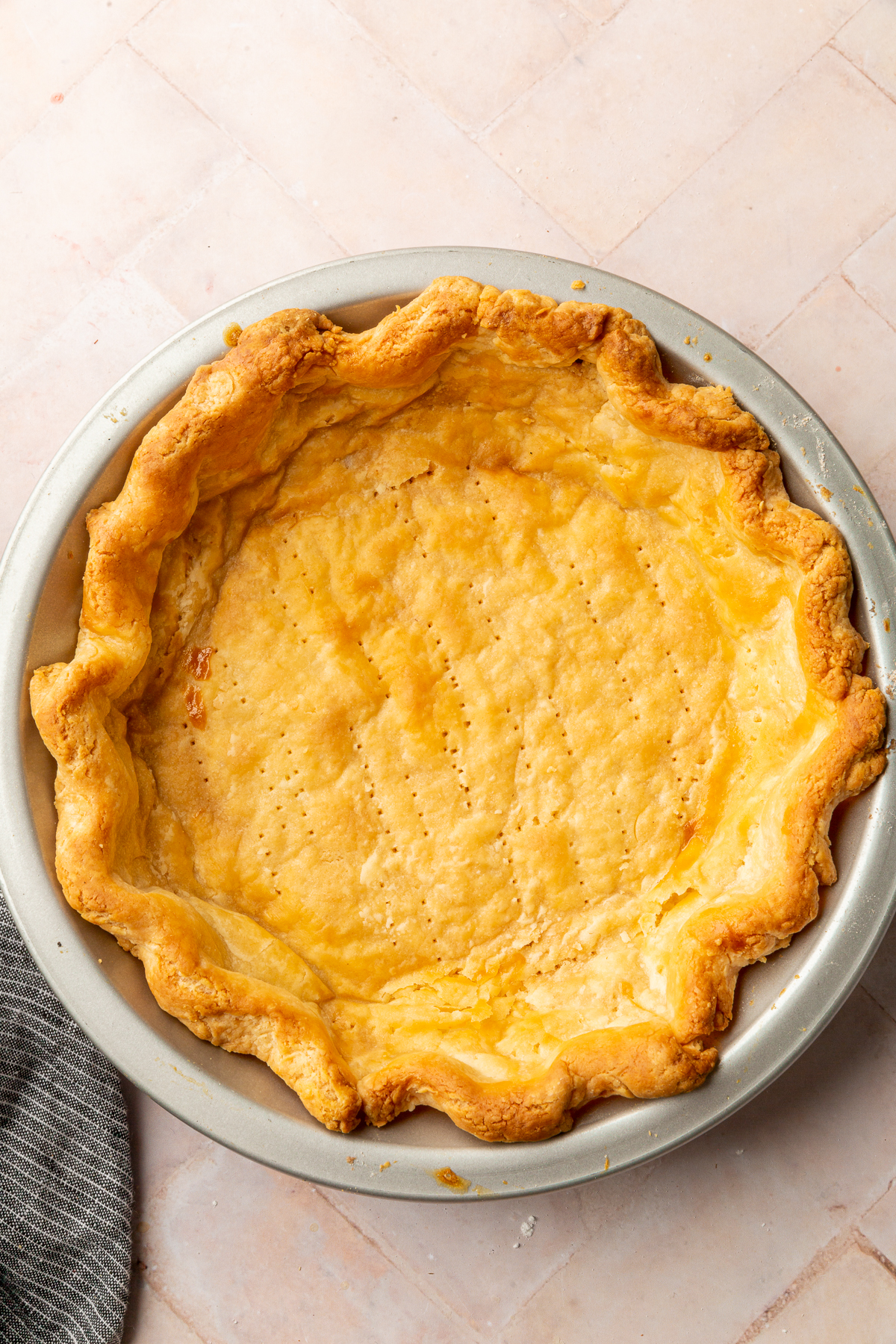 A golden-brown pie crust with fluted edges and small holes pricked on the bottom, ready to be filled.