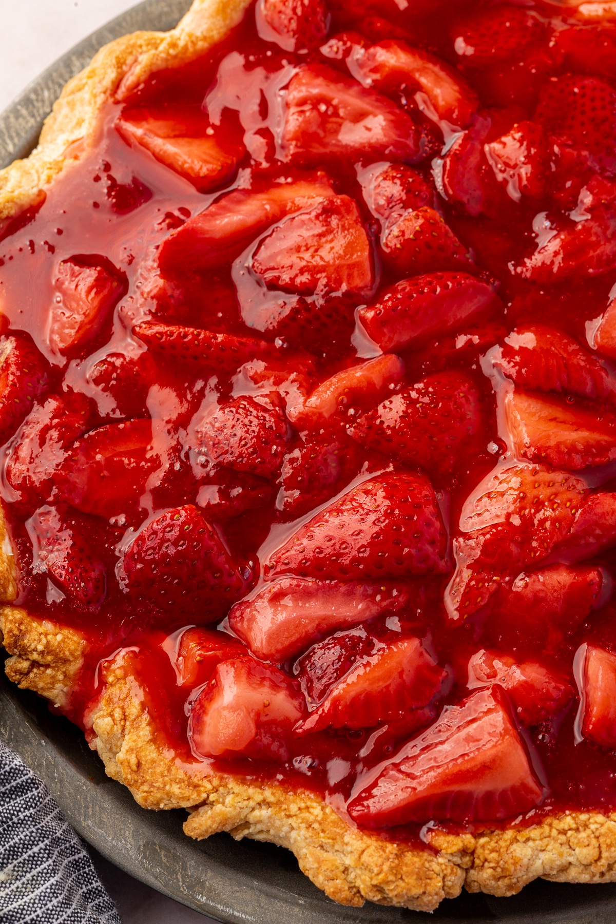 Bright red, glossy strawberry topping spread evenly over the cream cheese filling in the pie crust.