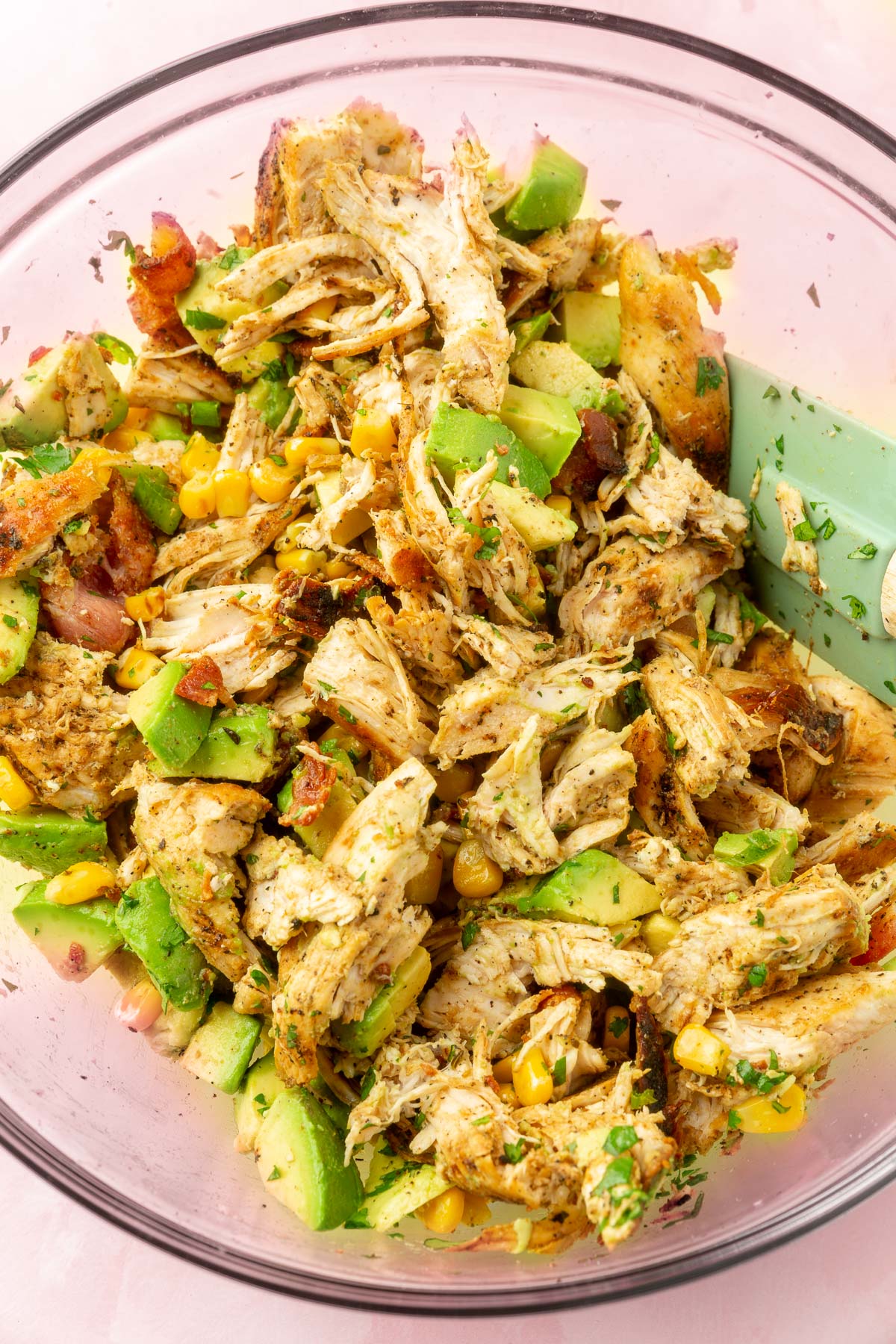 Ingredients for avocado chicken salad in a large mixing bowl in the process of being mixed.