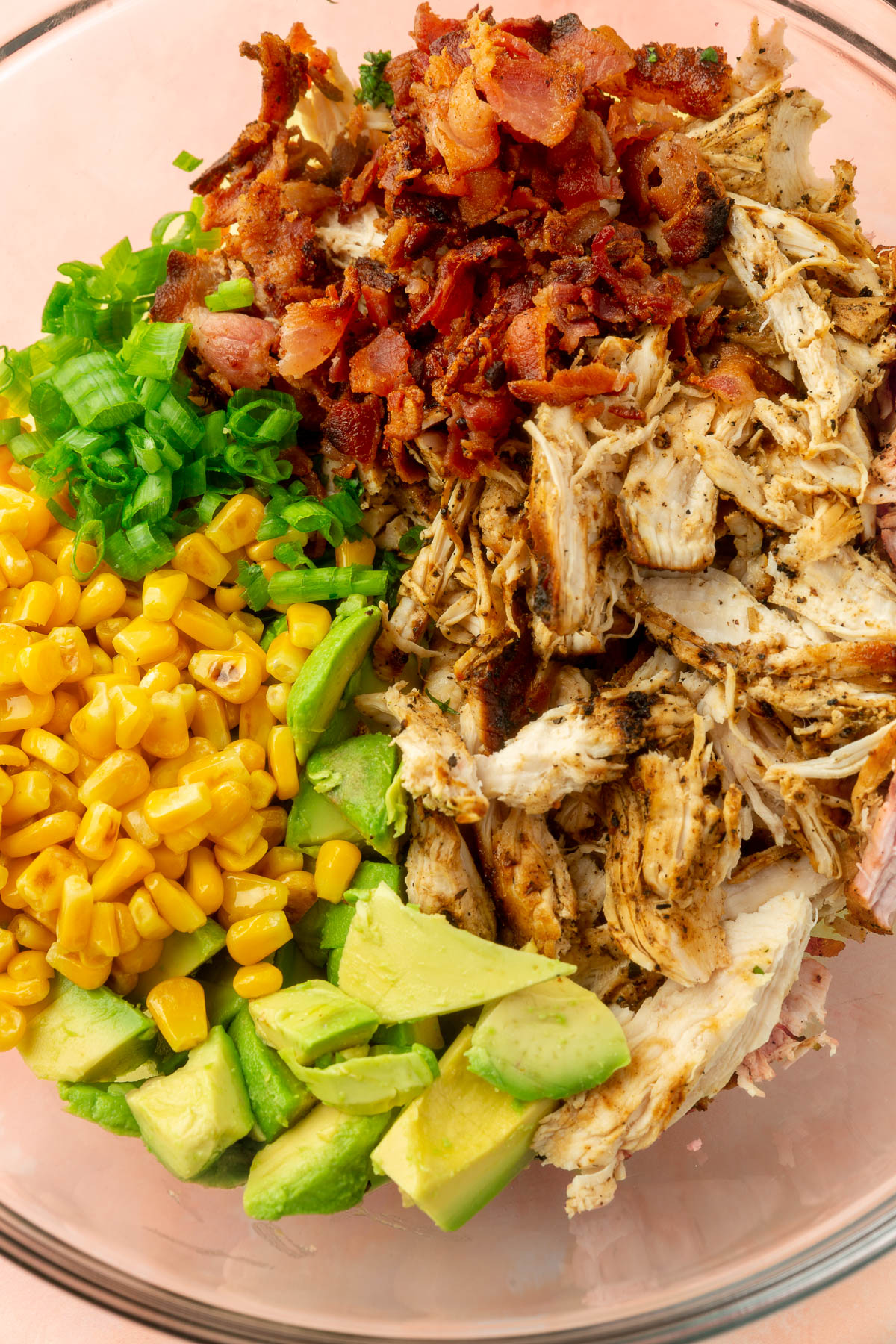 Cooked chicken, avocado, corn, green onions and bacon in a large mixing bowl not yet mixed together.