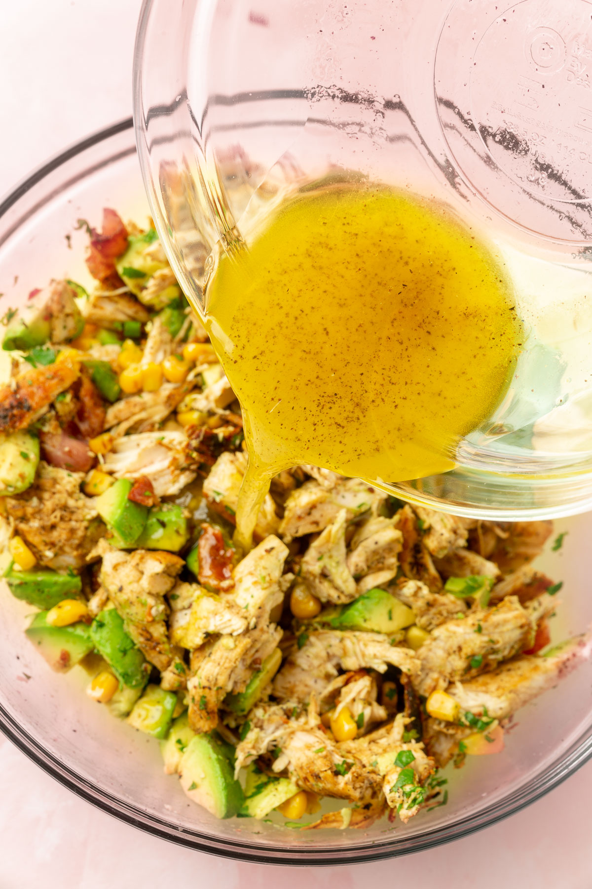 Dressing being poured over large bowl of avocado chicken salad.
