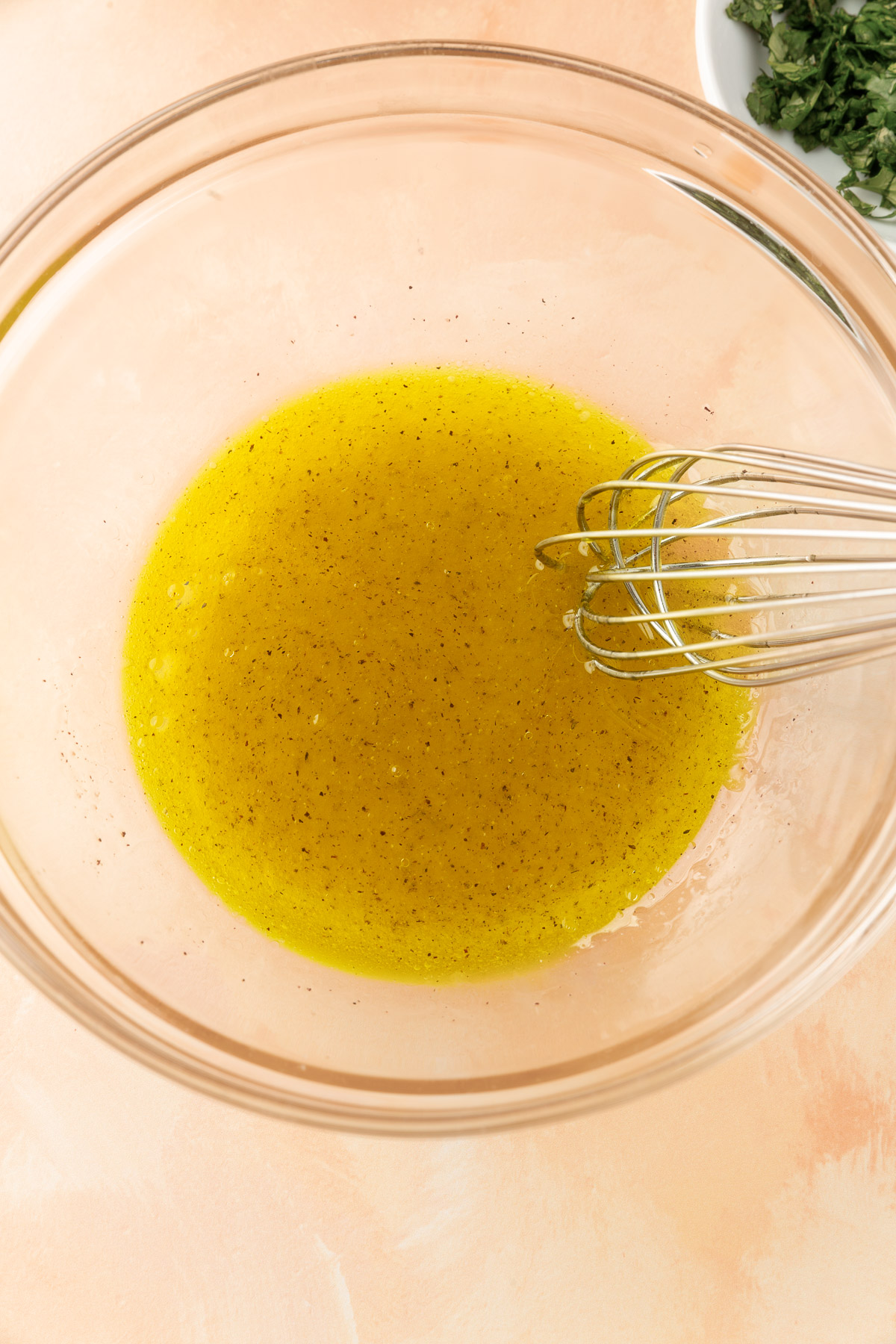 Image of making the dressing for the avocado chicken salad, the ingredients olive oil, lemon juice, salt and black pepper in a mixing bowl with a whisk.