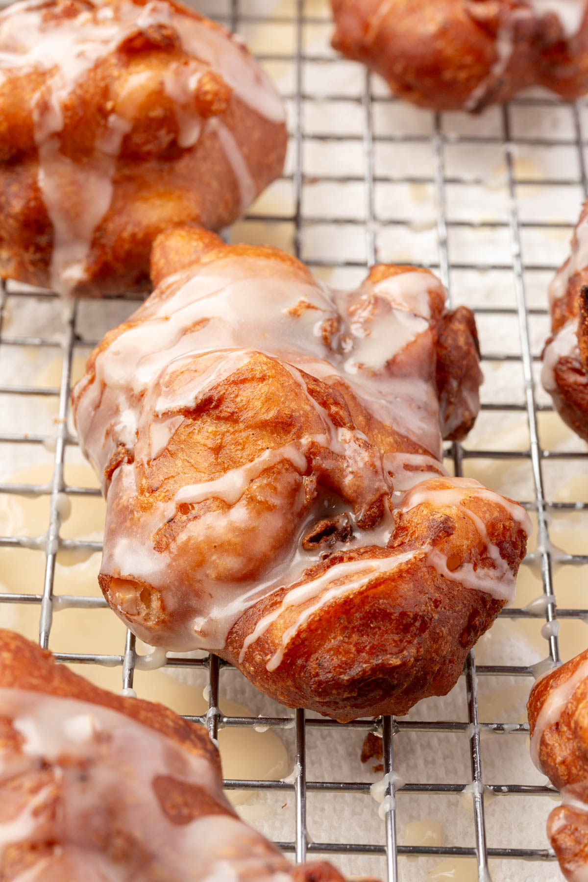 Gluten-free apple fritters cooling on a wire rack, each topped with a light glaze drizzle.