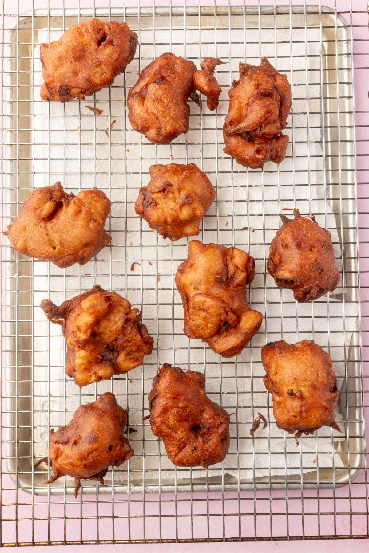 Fried gluten-free apple fritters on a cooling rack lined with paper towels.
