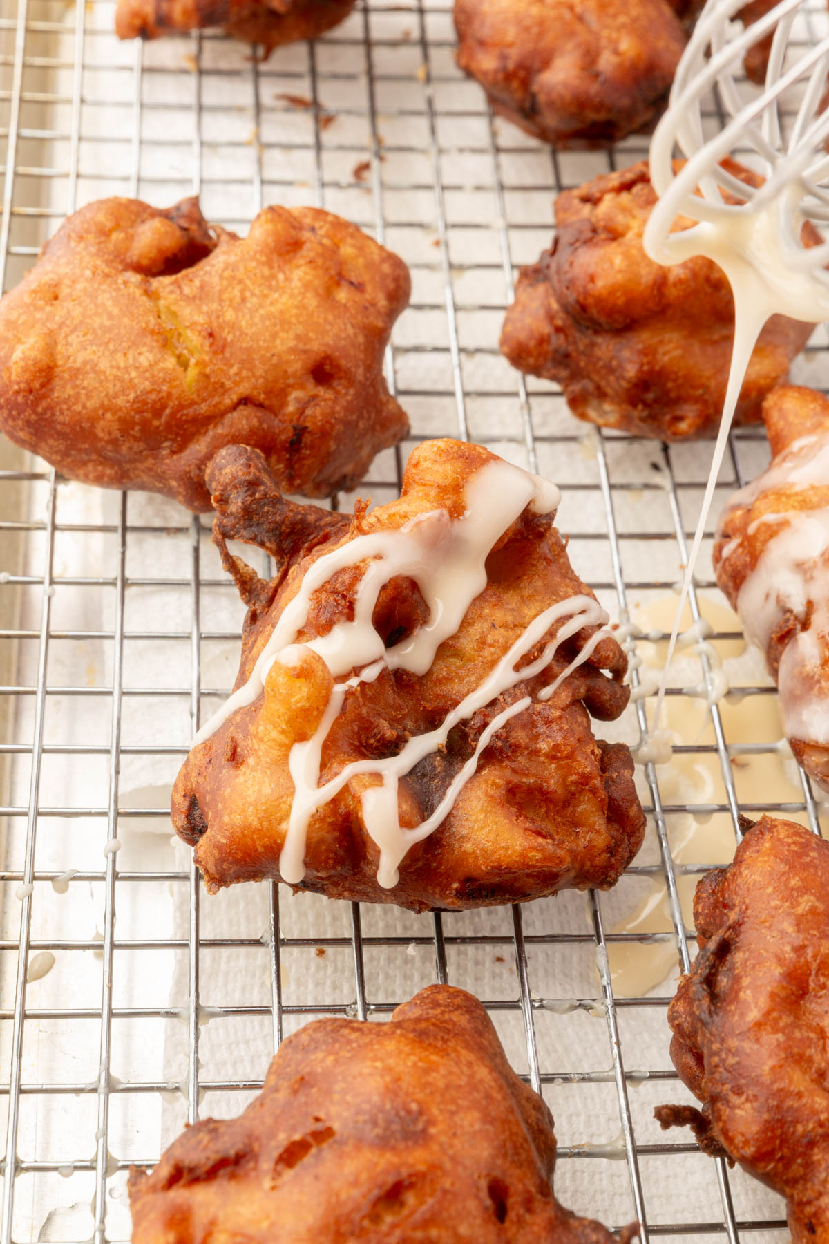 Drizzling glaze over freshly fried gluten-free apple fritters on a cooling rack.